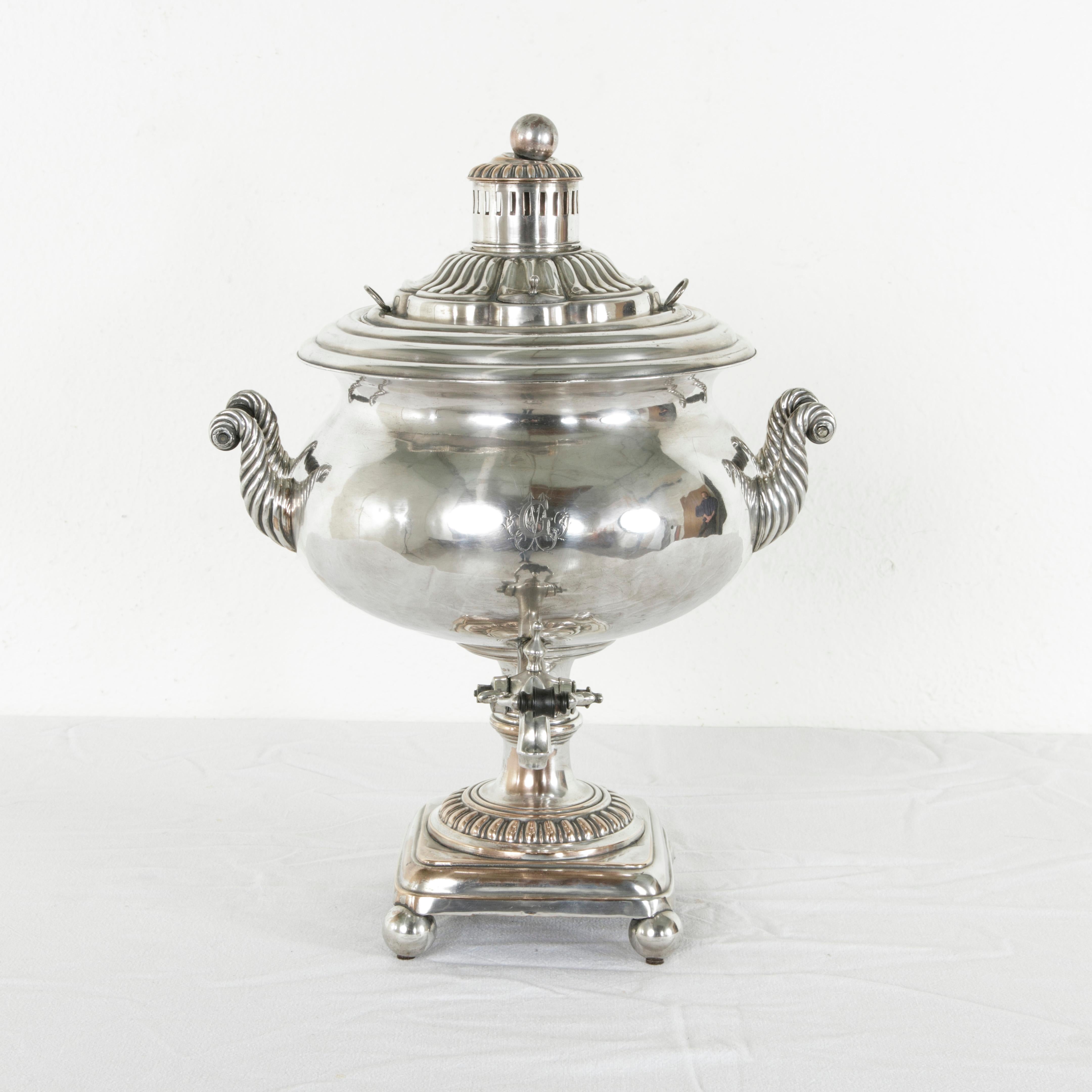 Originally used to serve tea, this late 19th century silver plate samovar or tea urn features an engraved monogram G surrounded by leaves above its serving spout. A scrolled handle on each side is fitted with an ebonized wooden bar that allows for