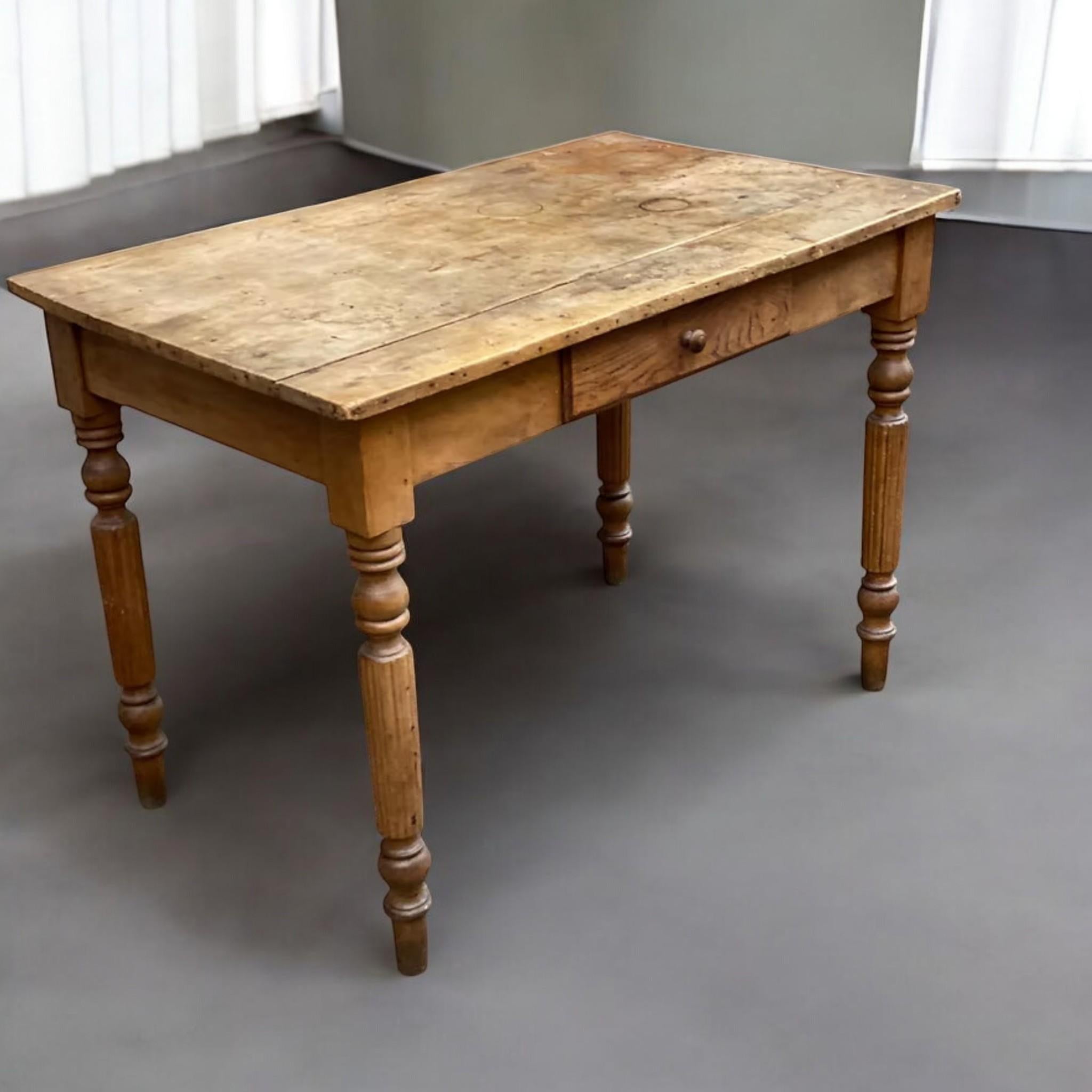 Questo affascinante tavolo rustico esemplifica l'eleganza pratica dell'artigianato rurale, probabilmente proveniente da una fattoria francese o inglese. Realizzato in pino massiccio, il pezzo presenta una superficie riccamente usurata con una patina