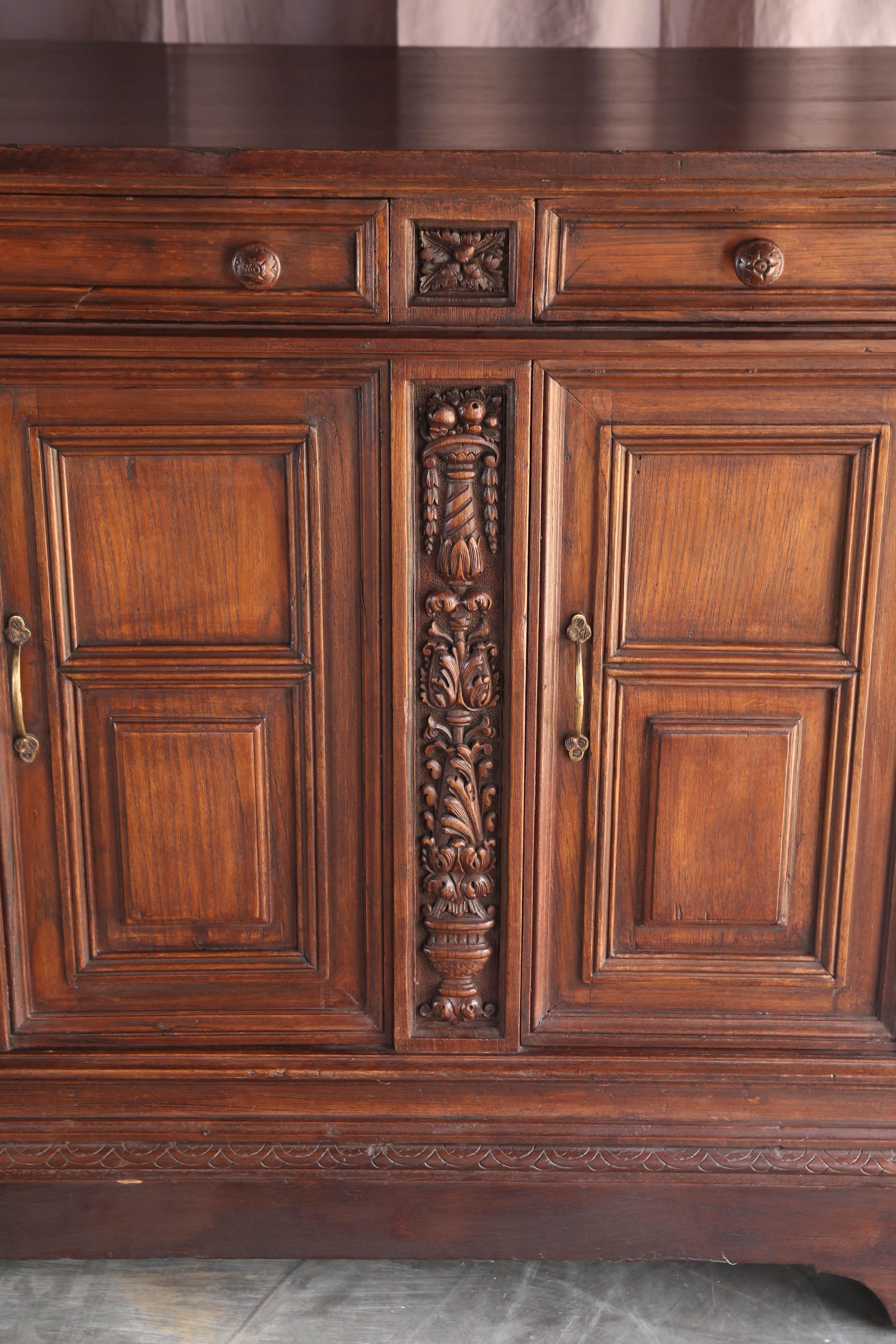 Very fine dense teak wood is used in making this unique entry hall piece. It comes from a French colony in Asia. The carvings on this piece are crisp and precise. It has three upper drawers and four doors for the shelves. It retains original cast