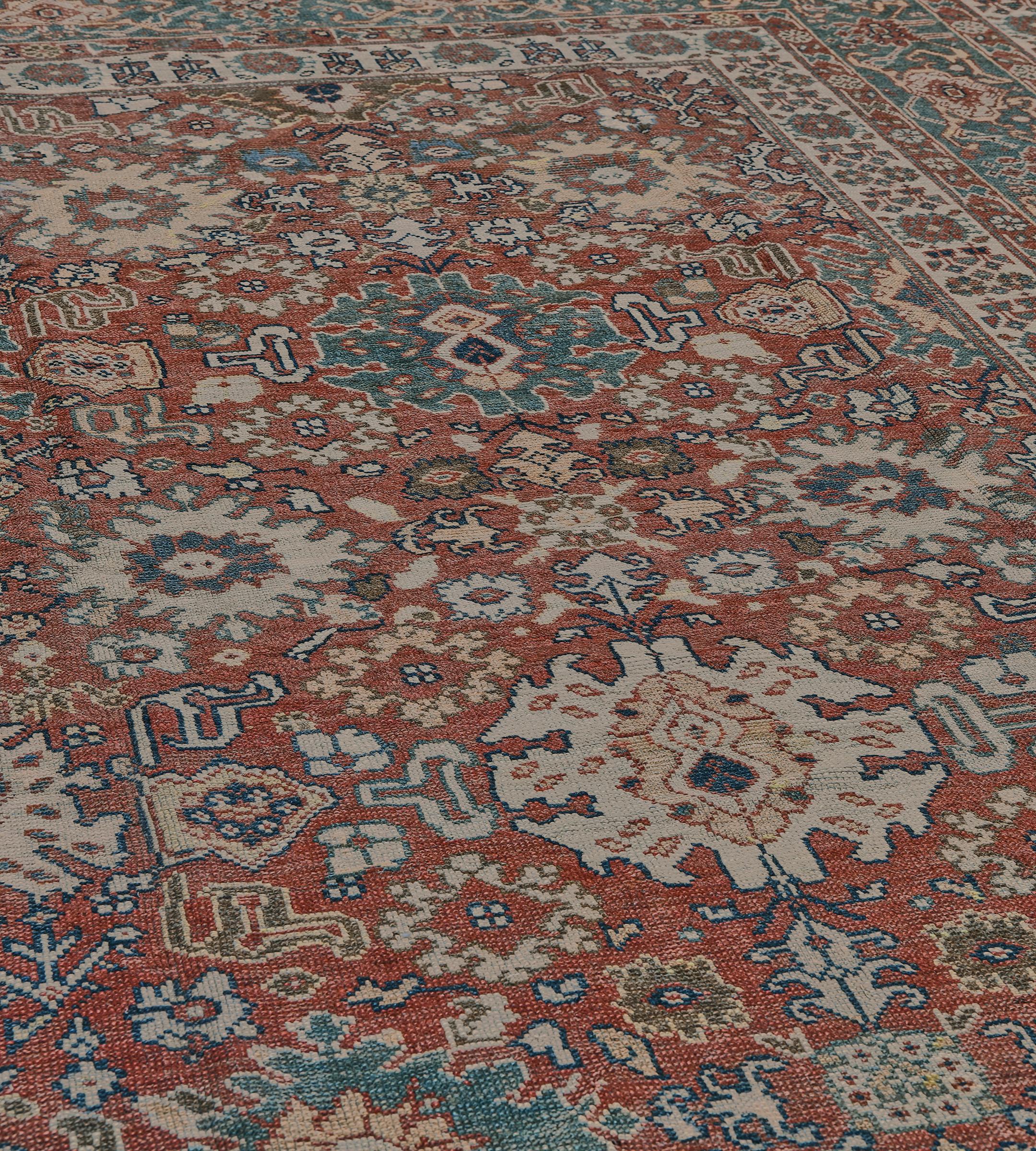 Questo tradizionale tappeto persiano Sultanabad Rugs, tessuto a mano, presenta un campo generale rosso ruggine con pronunciate icone a palmetta e raffinati motivi floreali, in un elegante bordo a palmetta di tartaruga blu acciaio, tra inaspettate