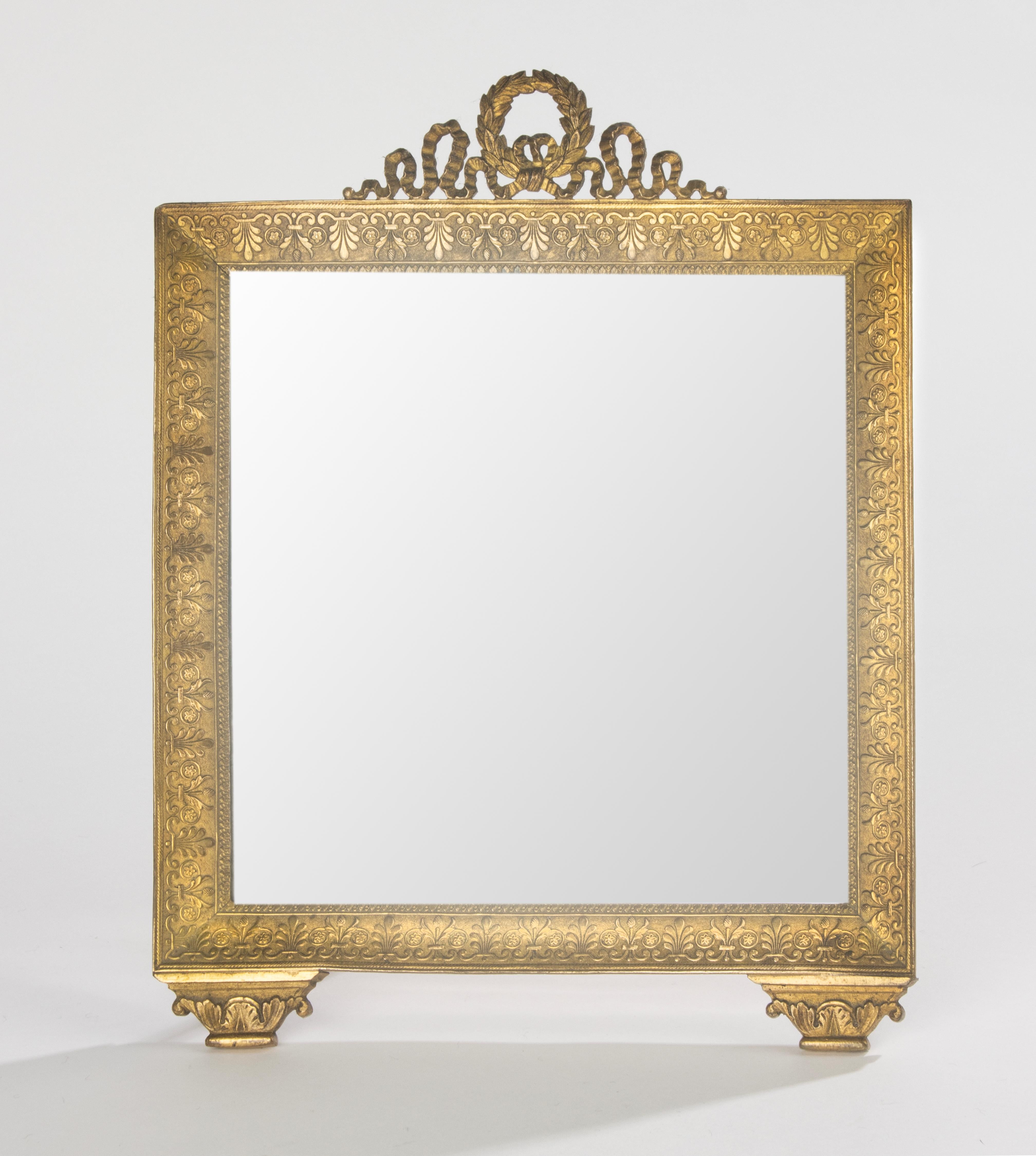 Charming French gilt bronze mirror, late 19th century, in Empire style. The rectangular frame is richly decorated with acanthus leaves and classical motifs, crowned with a laurel wreath and ribbon cresting. The piece rests on stylized feet,