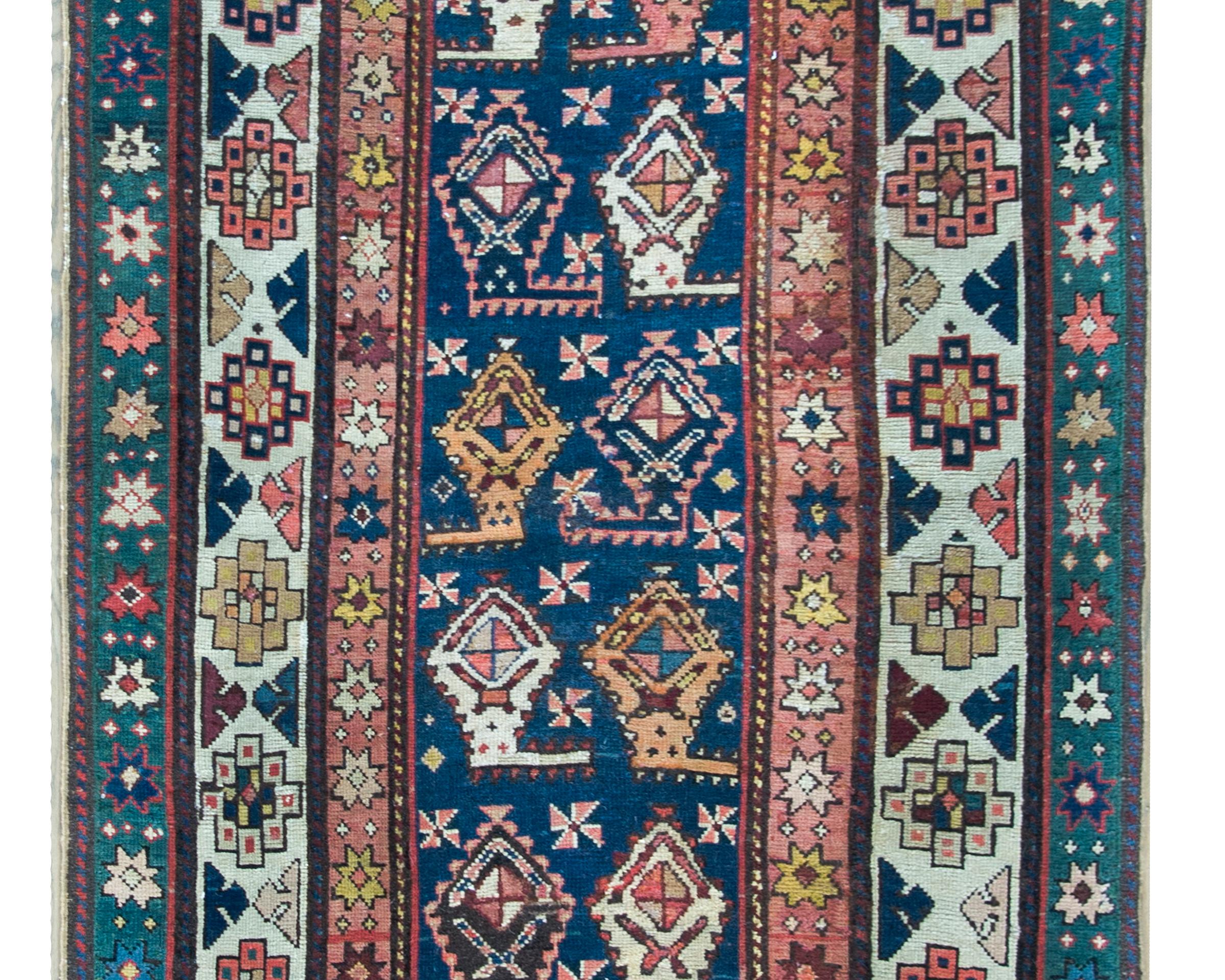 A remarkable late 19th century Azerbaijani Talesh runner with a repeated stylized paisley pattern woven in pinks, crimsons, white, golds and indigos set against a dark indigo background, and all surrounded by three distinct stylized floral patterned
