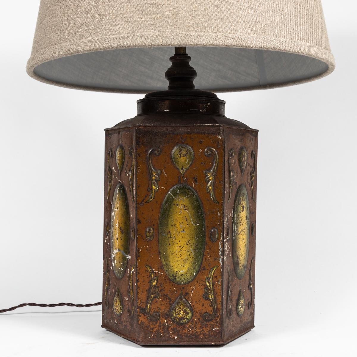 Late 19th-century English tole table lamp with deep rust and yellow hand-painted accenting and custom flax-toned linen shade. The hexagonal base features an oblong disc on each of its panels, surrounded by a few small architectural flourishes. The