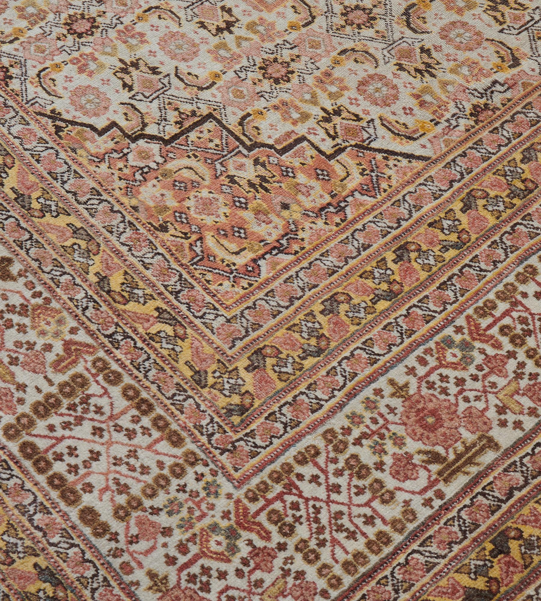 This traditional hand-woven Persian Tabriz rug has a refined ivory herati field interrupted by a stylized arabesque floral sub-field, enclosing a rust red arabesque lozenge medallion and with similar quarter spandrels, in a complementary dense