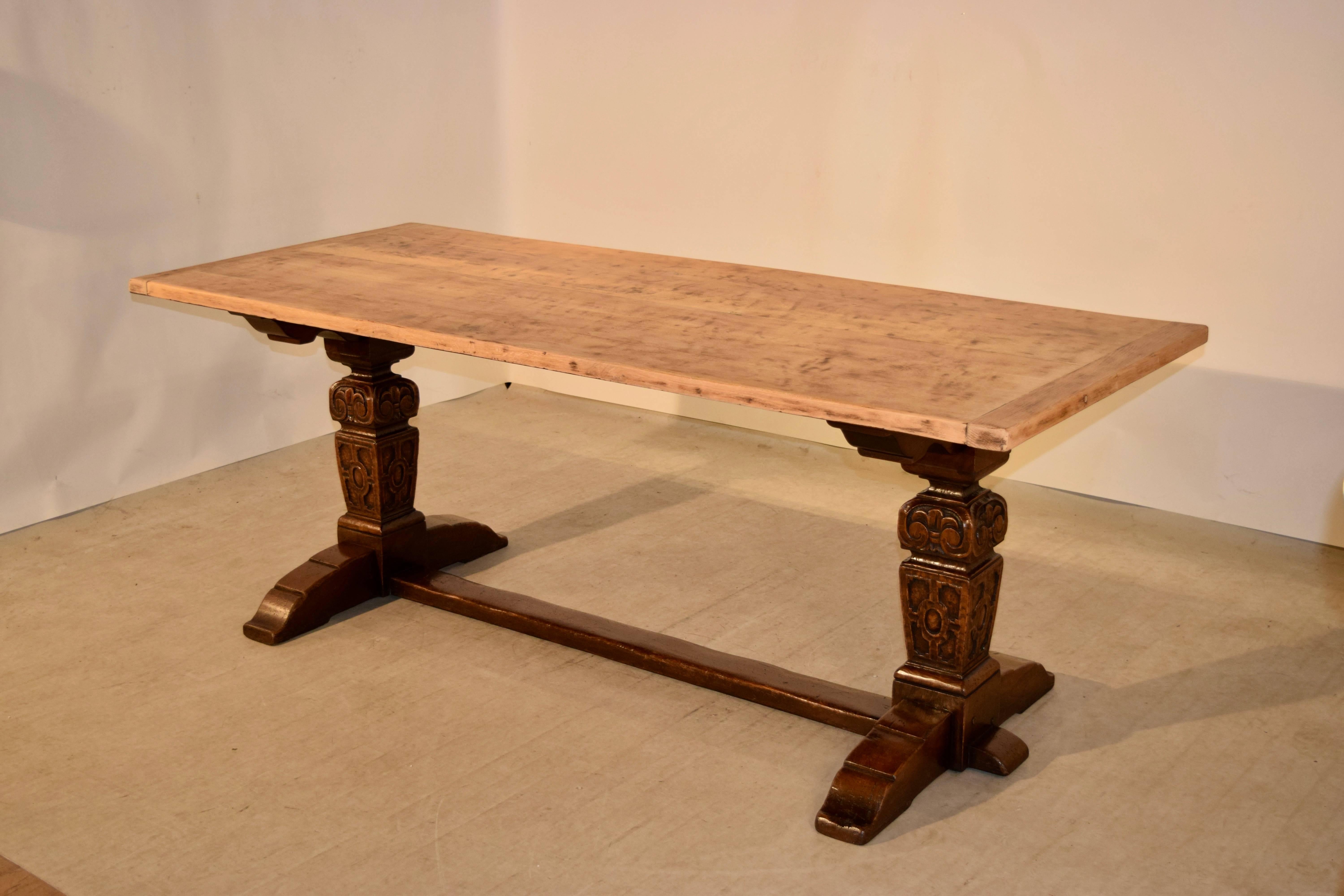 Late 19th century oak trestle table from England. The top is scrubbed to its natural color oak, and is wonderfully contrasted to the base. The legs are hand-turned square and carved decorated and are supported upon a trestle base with attaching
