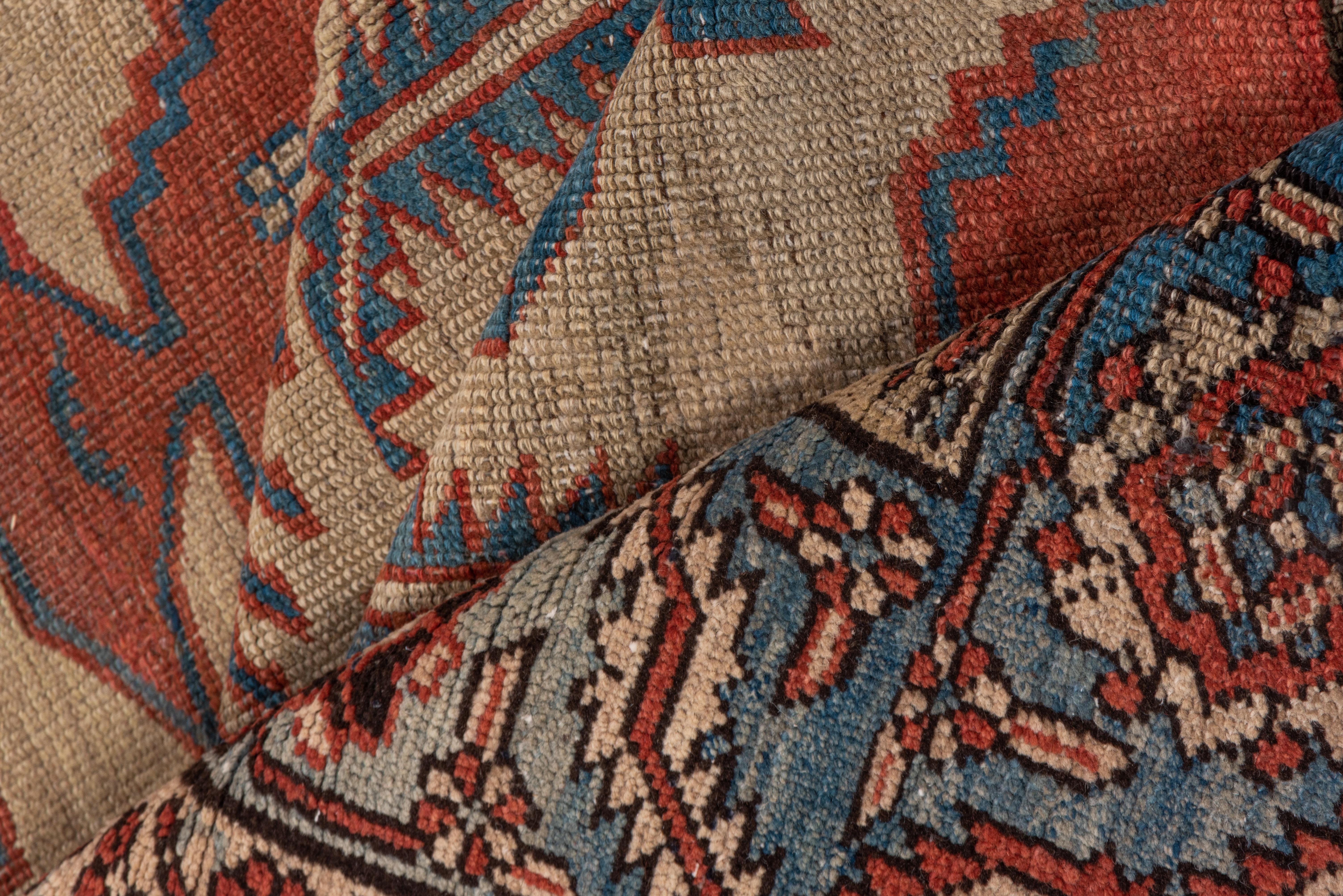 Ce tapis Heriz Serapi inhabituel présente un champ rouge garance chaud sur lequel sont disposées trois palmettes géantes super-stylisées, détaillées en crème et en bleu clair. La bordure principale bleu clair présente le motif populaire de rosette