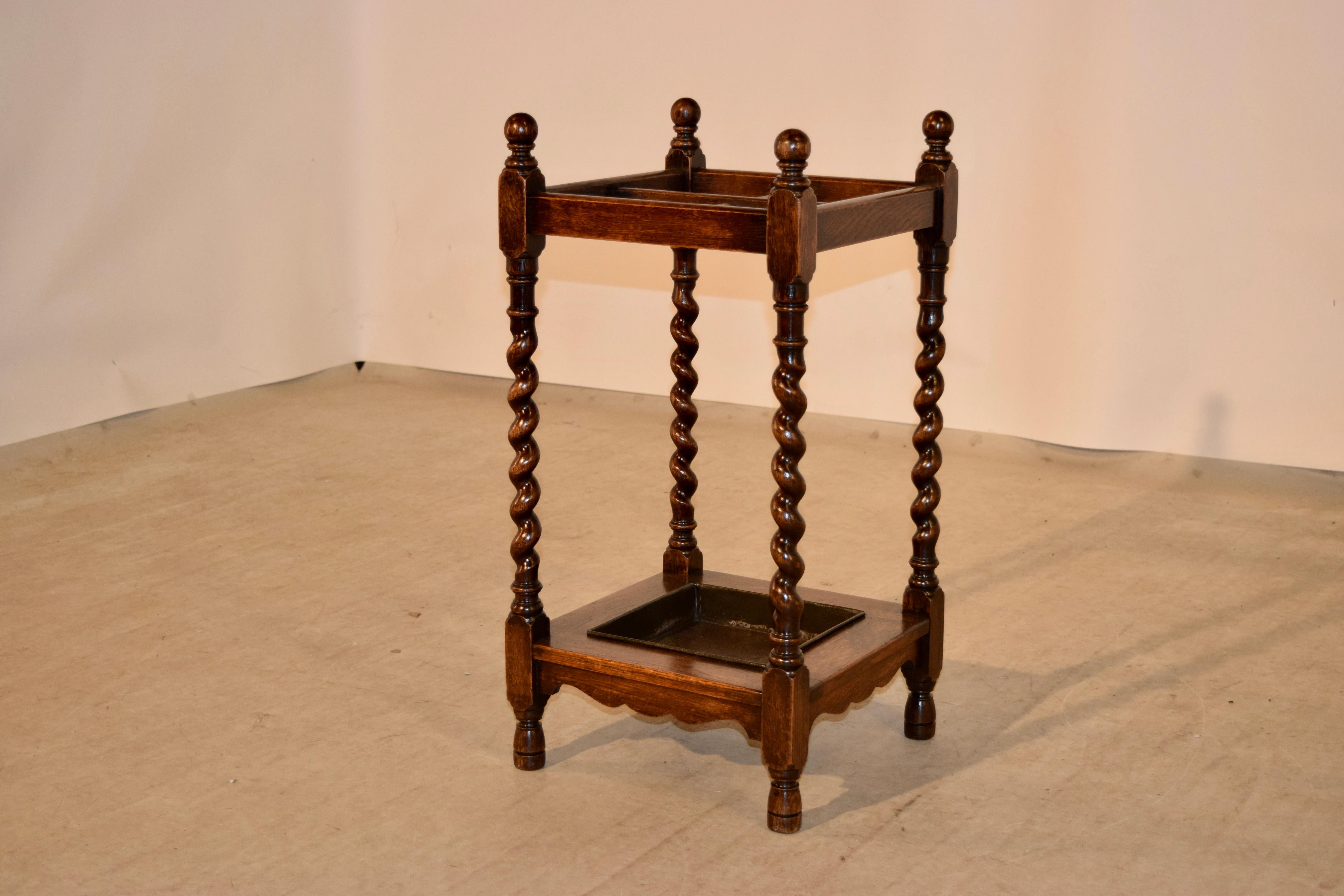 Late 19th century English oak umbrella stand with hand-turned barley twist legs, joined at the top by simple rails, with separations for umbrellas and canes, and joined at the bottom by scalloped rails which hold a painted metal drip tray. Raised on
