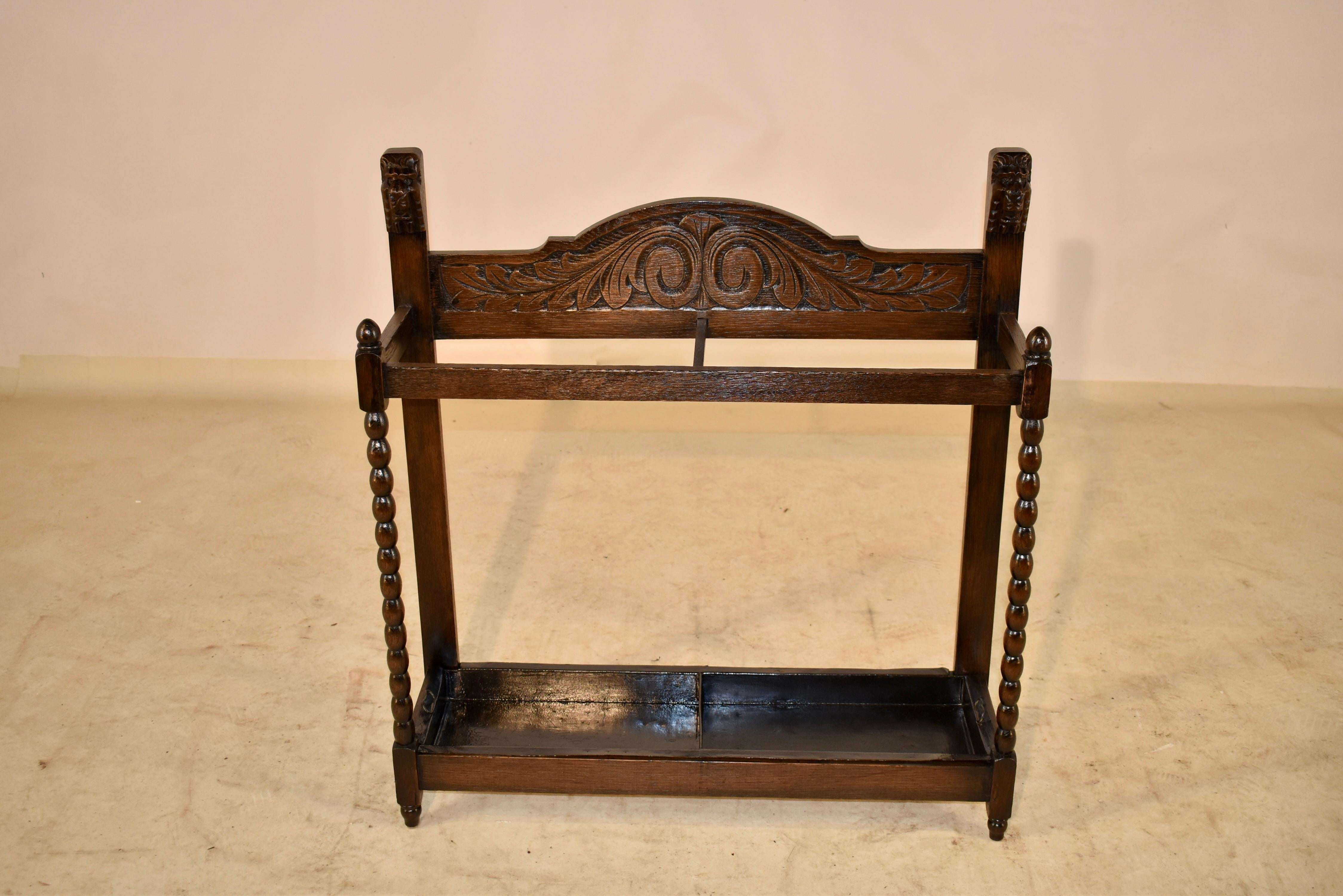 Late 19th century oak umbrella stand from England with hand carved decoration on the back, flanked by hand carved lion's heads. The front legs are hand turned in a bobbin design and the back legs are simple to fit easily against a wall. The original