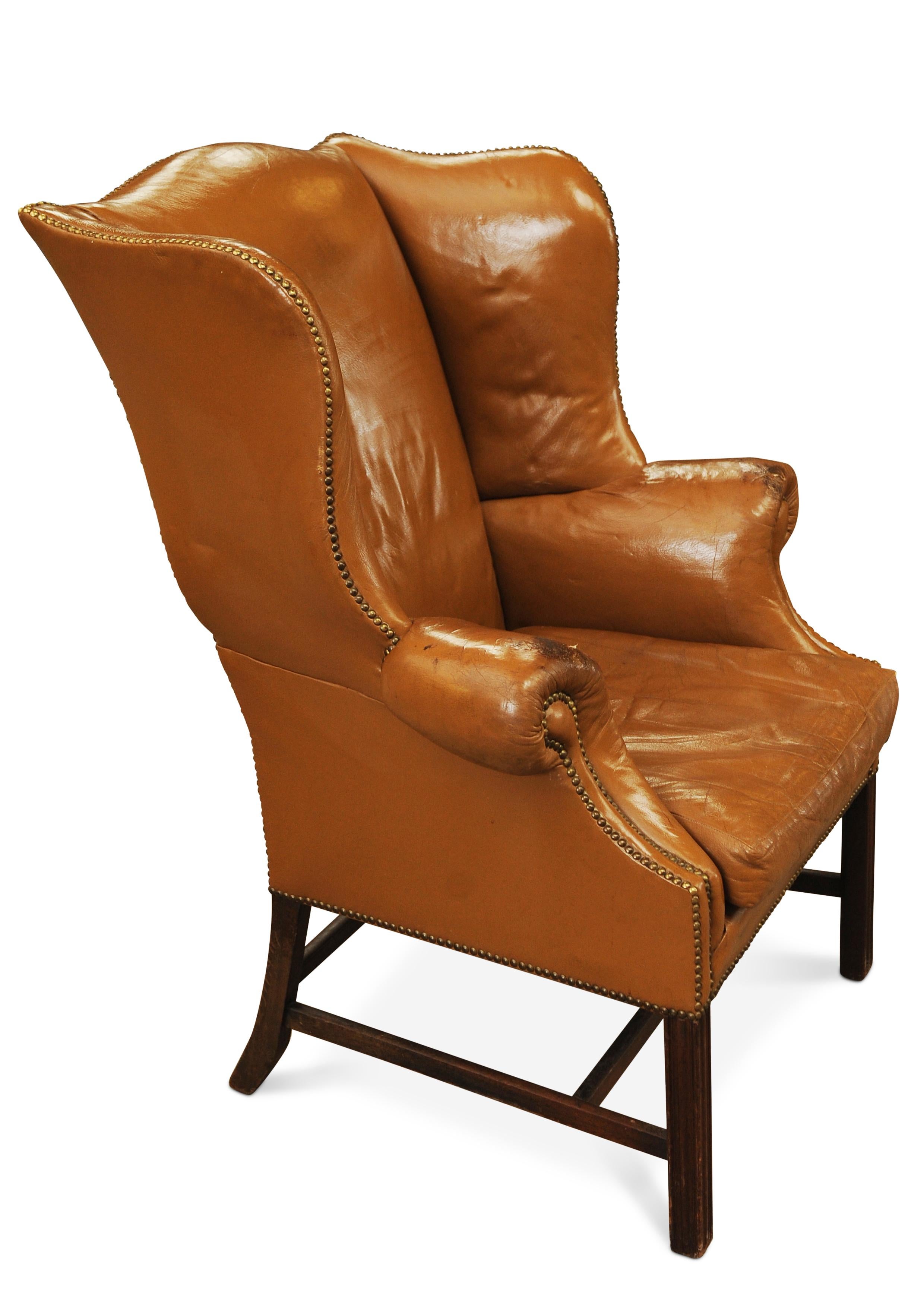 19th Century Georgian Mahogany And Tan Leather Wing Back Armchair With Brass Studded Border.

Featuring a shaped back with out-scrolled arms raised over squared fluted front legs, shaped back legs joined with H stretcher, upholstered in a tan