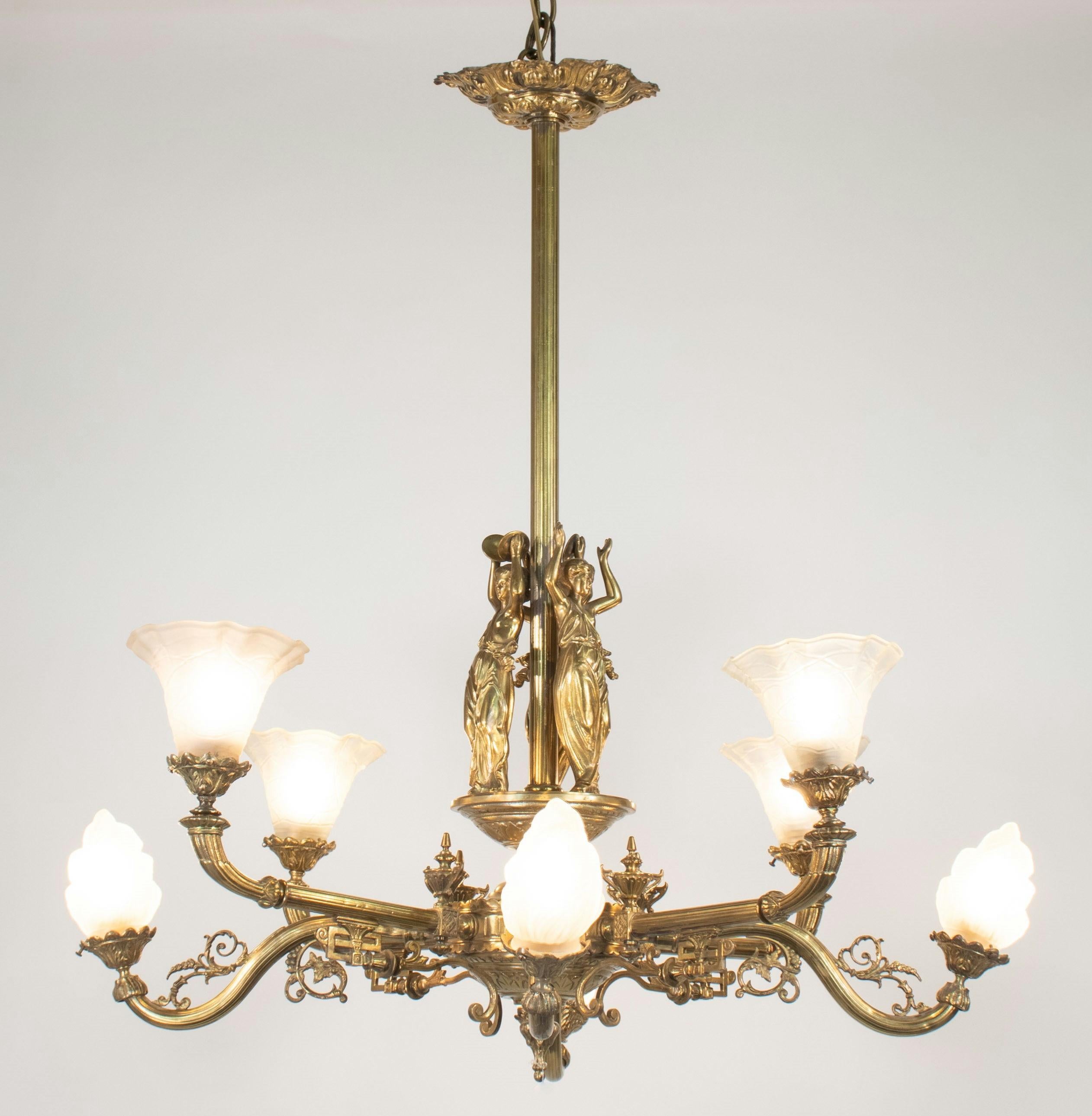 Questo squisito lampadario della fine del XIX secolo fonde magistralmente l'estetica vittoriana e neoclassica, realizzato in bronzo con otto accattivanti luci. I paralumi in vetro acidato sono disegnati artisticamente, con quattro che assomigliano a