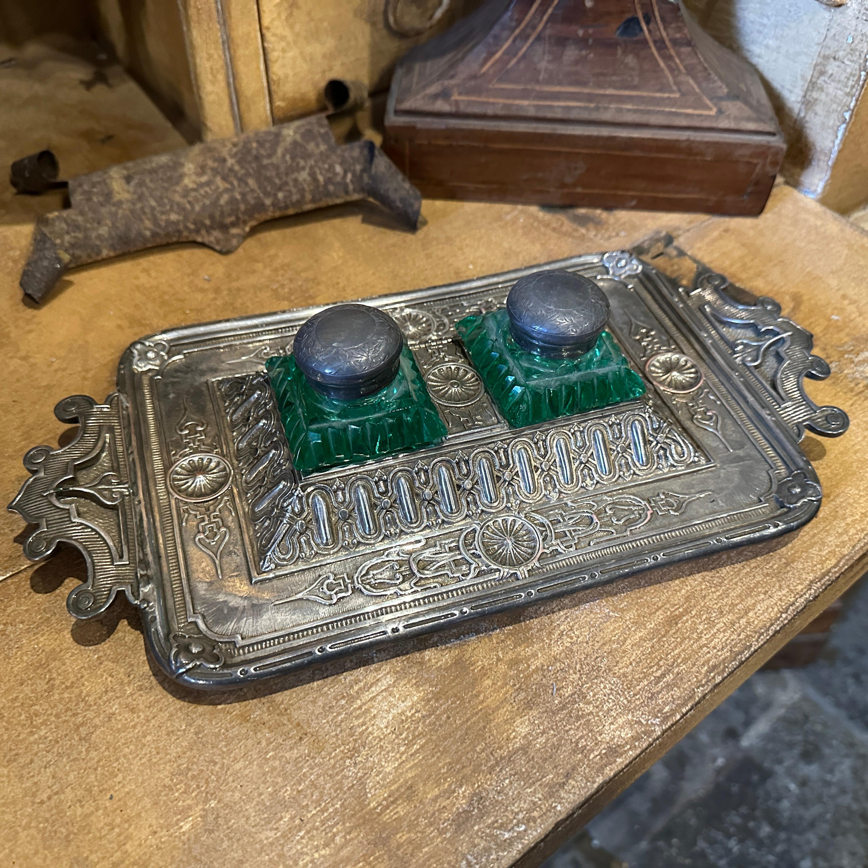 This Late 19th Century Victorian inkwell set exemplifies intricate craftsmanship and luxurious design. It features a silver-plated tray with ornate detailing, including embossed floral patterns, geometric motifs, and scrolling edges that showcase