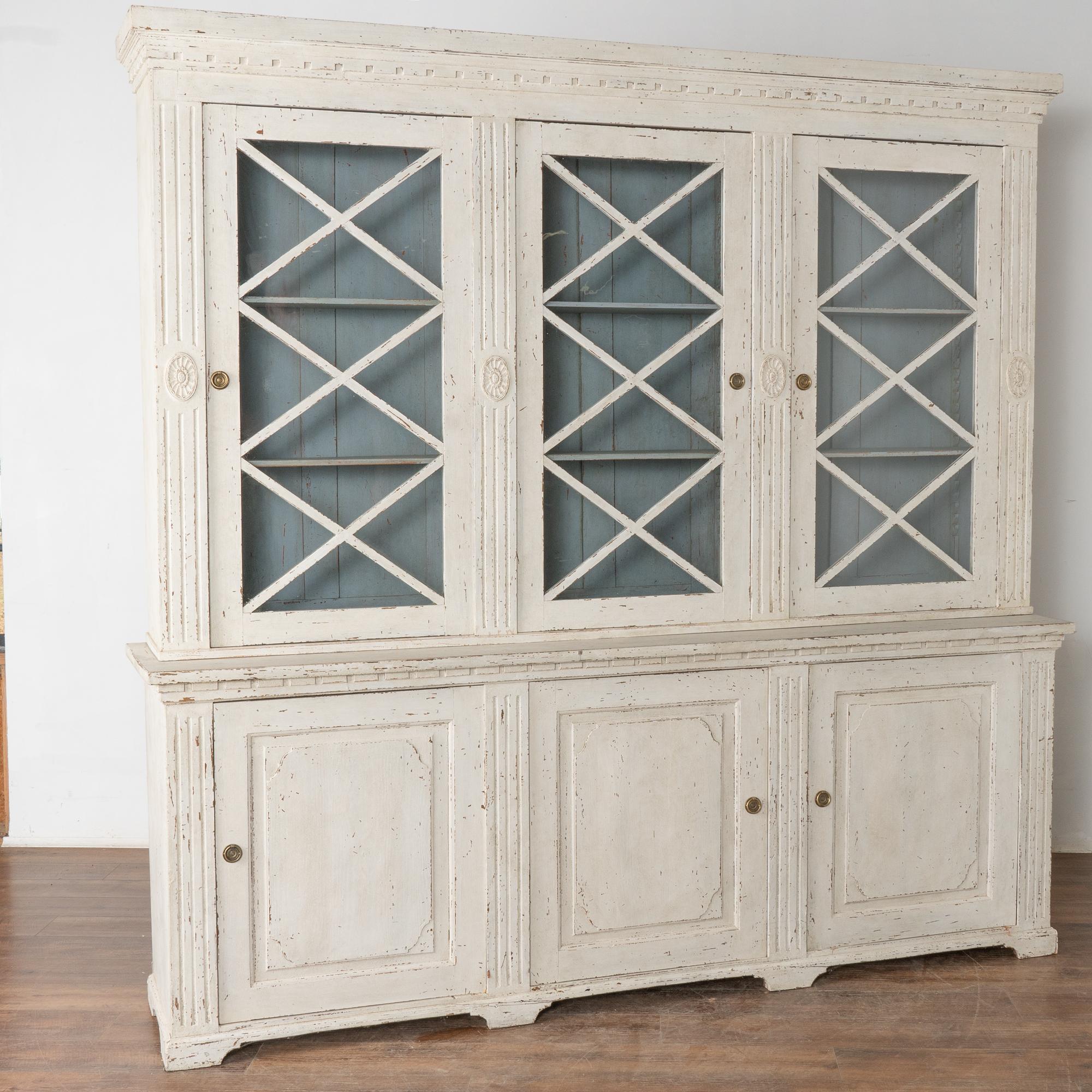 Elegant and stately Swedish Gustavian style display cabinet or bookcase in two sections standing just over 7' tall and 7' wide.
Newer professional painted finish in antique white which has been softly distressed fitting the age and grace of this