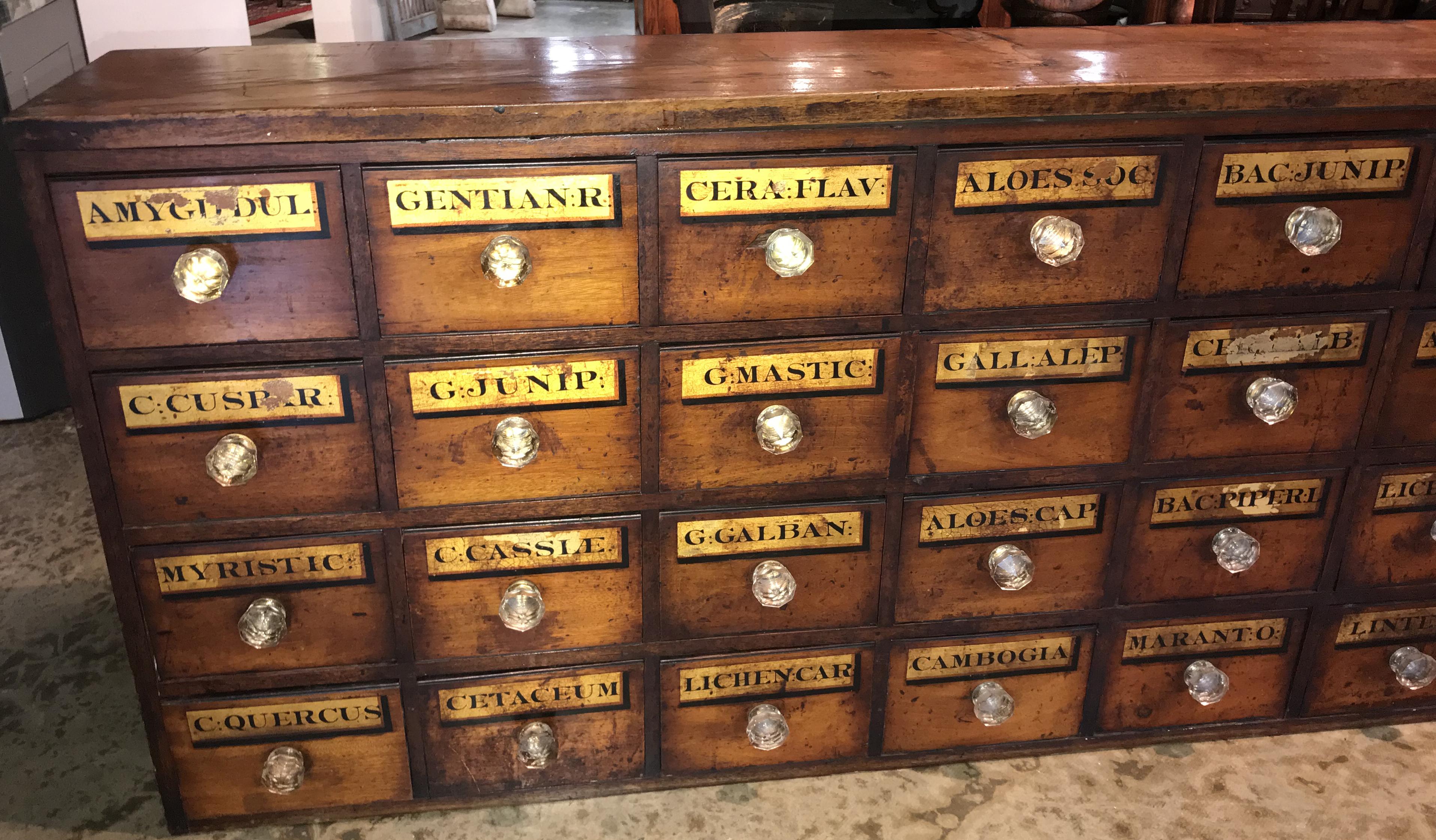 A fine wooden 32-drawer chemist apothecary chest with glass knobs, each drawer labeled with black on gold with names of chemicals or potions used at the time. Some hand inscribed labels can be found on the interior of the drawers. There is no back