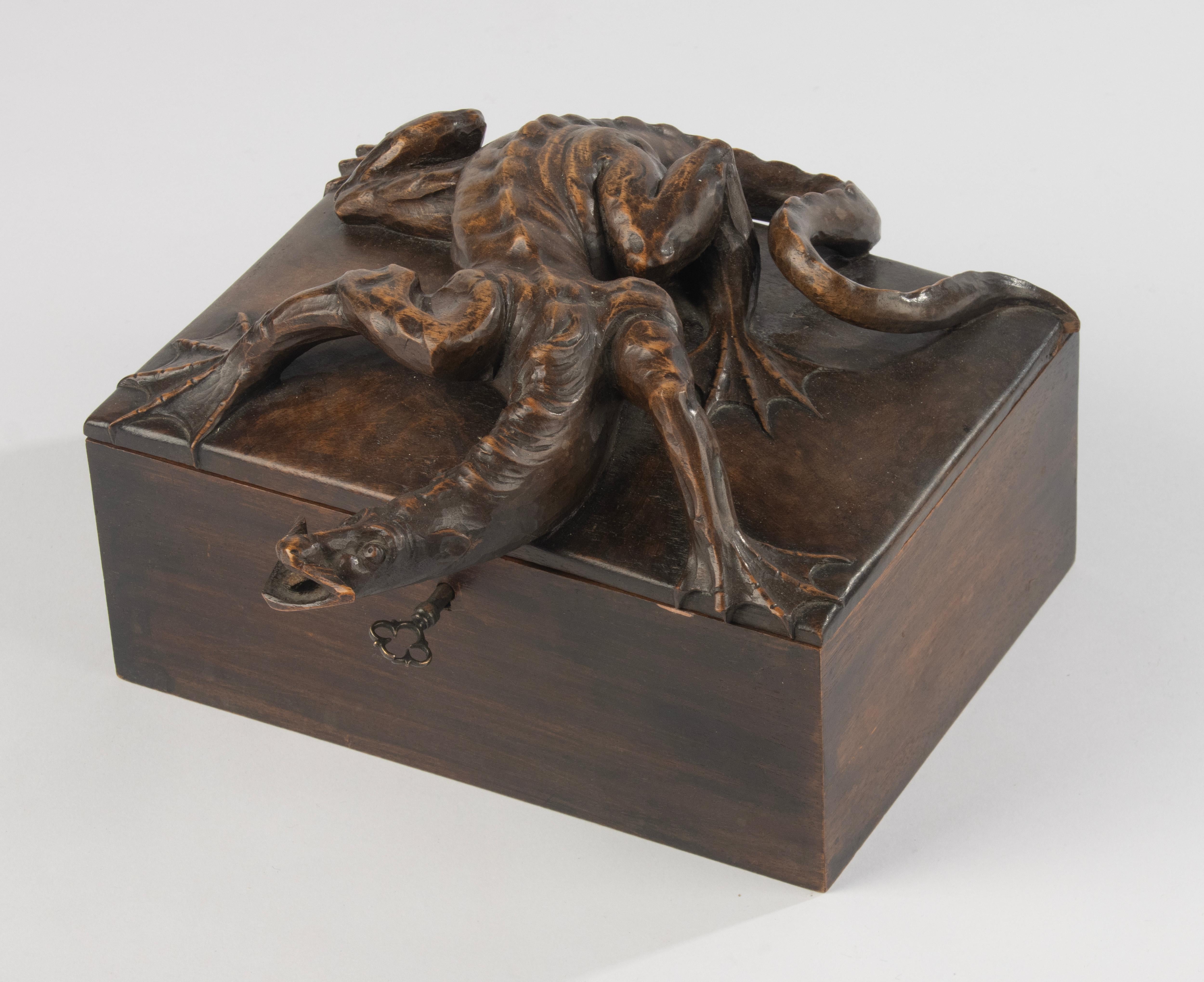 Magnifique et inhabituelle boîte en noyer de la Forêt-Noire, datant de la fin du XIXe siècle, finement sculptée d'une créature grotesque ressemblant à un dragon sur le couvercle. La sculpture est très détaillée, avec une musculature prononcée et des
