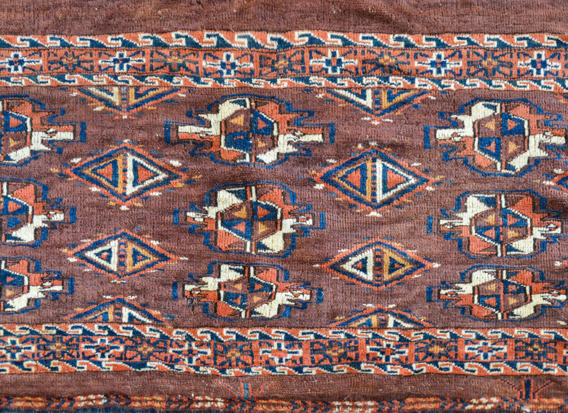 Tapis persan Yamout de la fin du XIXe siècle composé de multiples médaillons floraux stylisés tissés en cramoisi, blanc, indigo et orange, sur un fond brun, et entouré d'une magnifique bordure contenant des fleurs stylisées flanquées d'une paire de