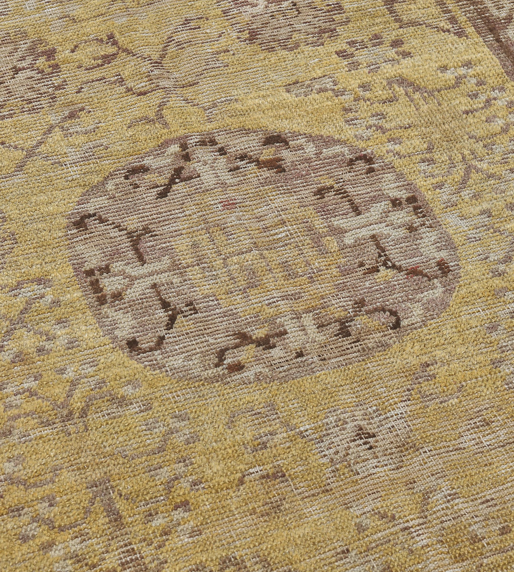 This antique Khotan rug has a golden-yellow field with a central pomegranate shaped lozenge of shaded purple surrounded by delicate flower-heads and floral sprays with open angular stepped spandrels, in a shaded purple border of spaced polychrome