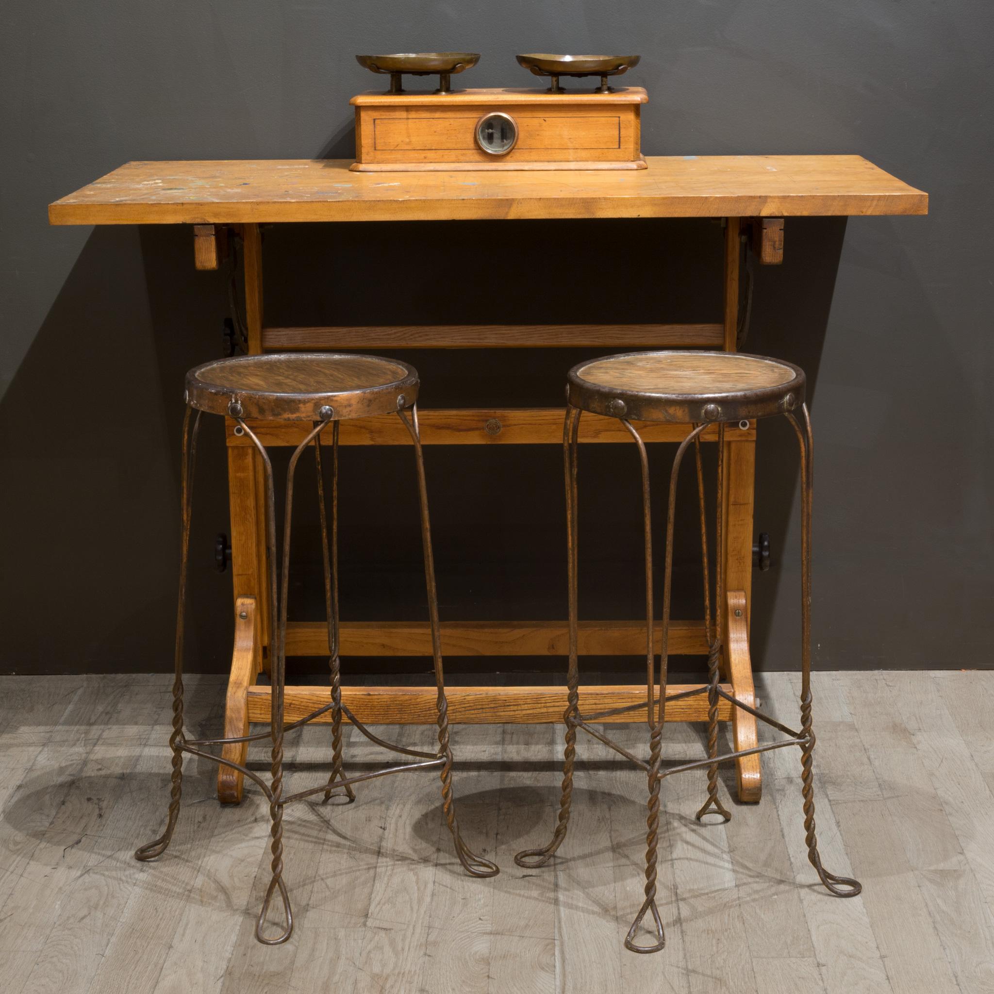 A pair of original antique American four-legged wrought iron ice cream parlor or soda fountain stationary bar stools. The chairs are comprised of heavy gauge wrought iron with a copper plate. The twisted and hooped feet are structurally sound and