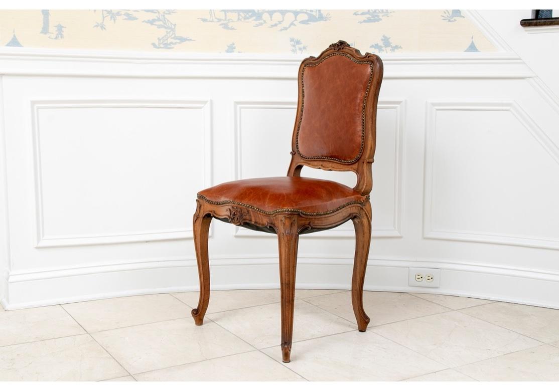 An elegant and fine set with two arm and twelve side chairs. Finely carved walnut Louis XV style with deep Saddle tome leather upholstery and nailhead trim. With floral scrolled crests and the seat rails with carved leafy scrolls, the legs ending in