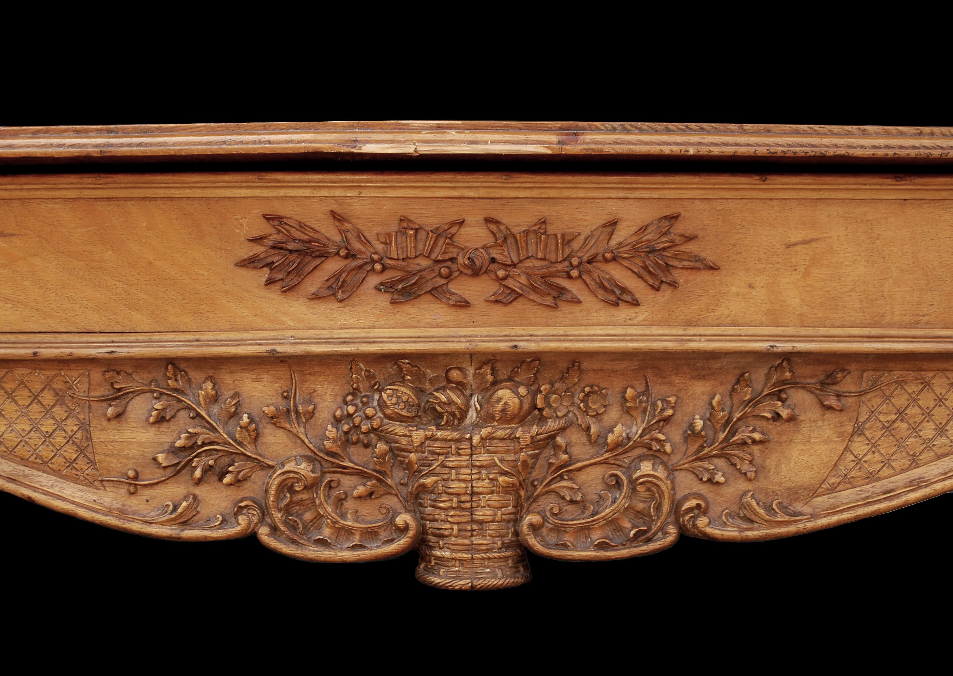 A late 19th-early 20th century English carved wood fireplace. The shaped frieze with basket of fruit and foliage surmounted by laurel leaves. The panelled jambs with bellflower husks tied by ribbons with inner carved egg and dart moulding. Photo