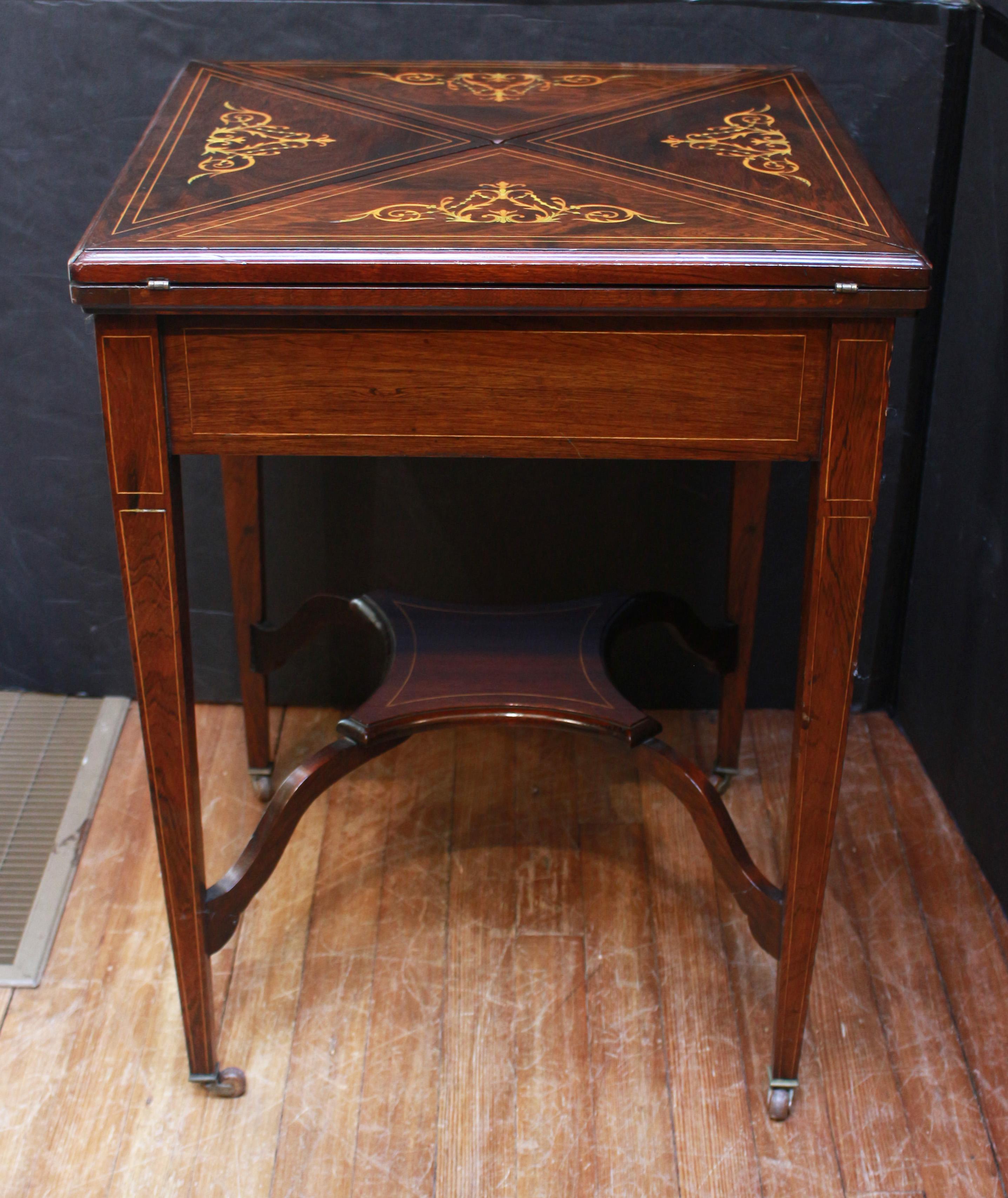Late 19th-early 20th century English handkerchief form games table. Late Victorian to Edwardian era. Mahogany with rosewood veneers and boxwood stringing. In the neoclassical revival taste with inlay of urn and flowers. Graceful arched stretchers to