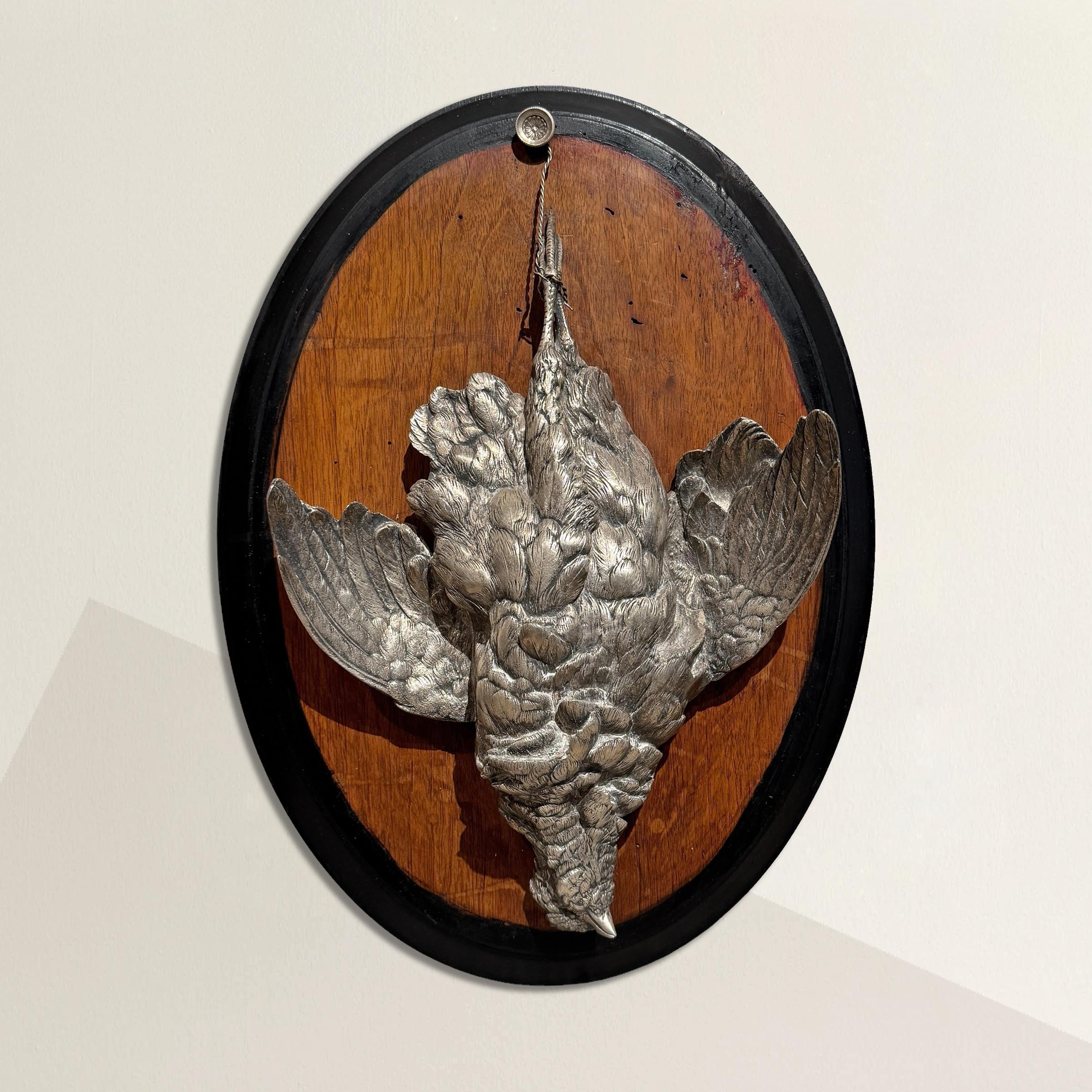 A striking blend of naturalism and ceremony, this late 19th to early 20th century German hunting trophy features a life-size grouse, cast in full dimension and silver-plated to gleam with quiet dignity. The bird hangs upside down by its feet,