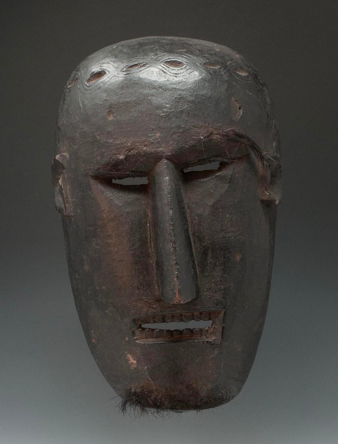 Late 19th-early 20th century Tribal mask, West Nepal

A mask from West Nepal with a sharp straight nose, squinting eyes and a square mouth showing upper and lower teeth. There are remnants of applied hair on the chine and near the eyes. Across the