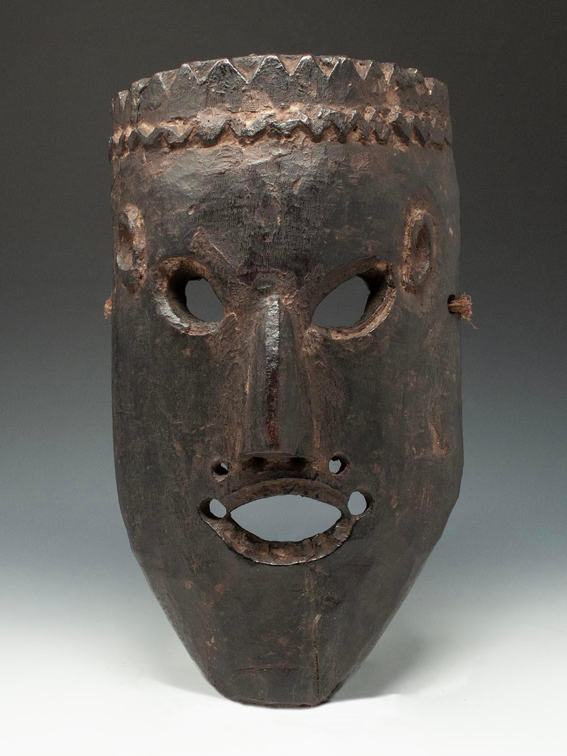 Late 19th-early 20th century Tribal mask, West Nepal

A mask from West Nepal with slanted almond shaped eyes, very small ears and an oval mouth showing carved upper and lower teeth over a strong squared chin. There is a jagged crown carved around
