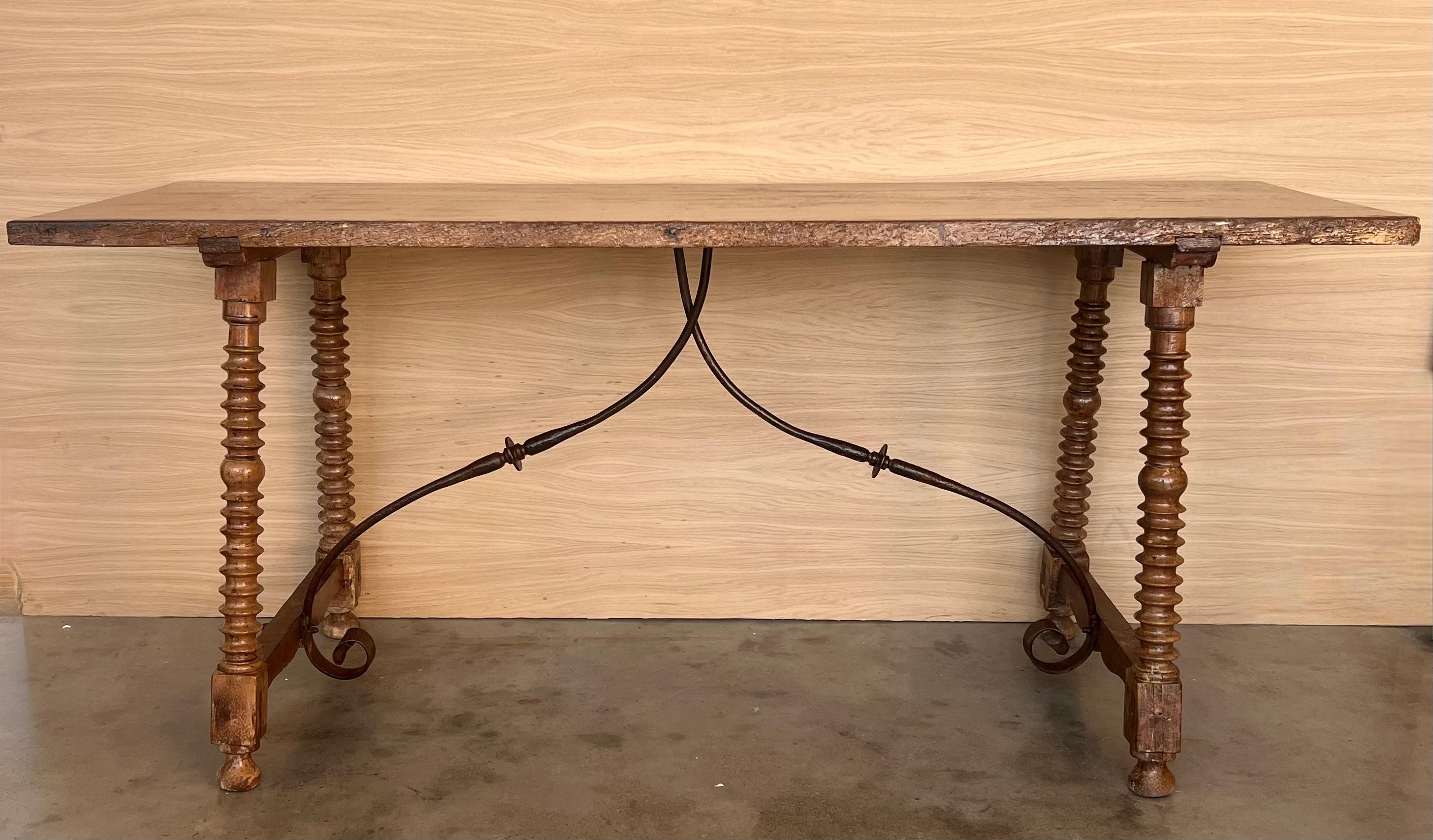 A Spanish Fratino dining table with hand made wrought-iron stretcher from the late 19th century. This Spanish wooden table features a sturdy rectangular top sitting above an exquisite base made of splayed carved legs connected to one another with a