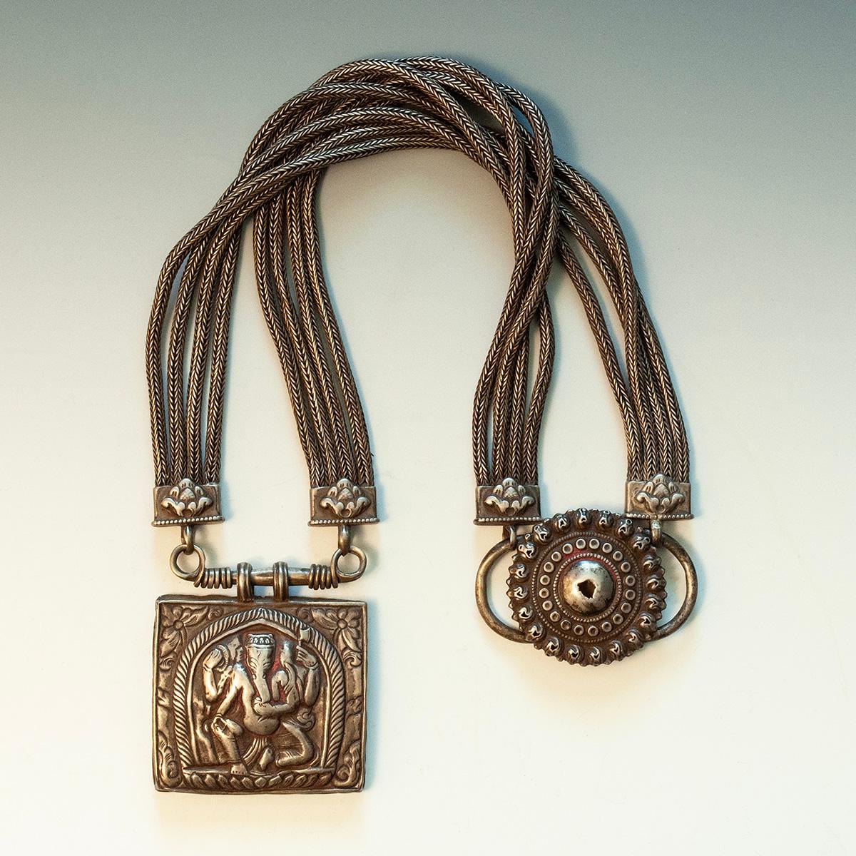 Collana Jantar del XIX-inizio XX secolo, Nepal

Questa lunga collana in lega d'argento (kakar-manka), detta jantar, presenta una scatola amuleto cava raffigurante il dio elefante Ganesha, che è sospesa a otto corde d'argento intrecciate, ancorate