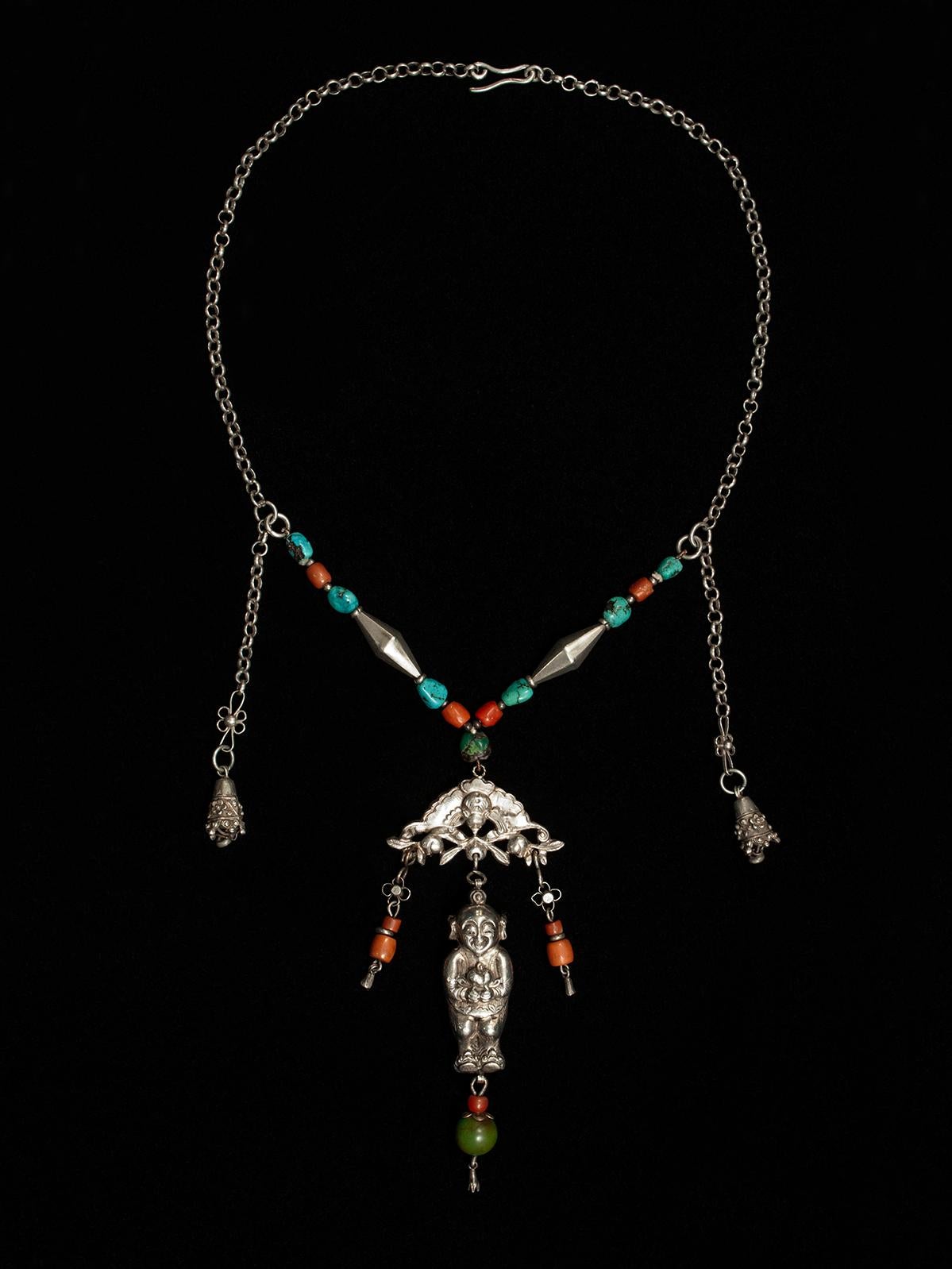 Late 19th to early 20th century silver baby amulet necklace, China

A wonderfully balanced silver chain necklace with coral and turquoise beads is anchored by a bat, from which dangles a baby amulet holding what appear to be peaches. 

The inner