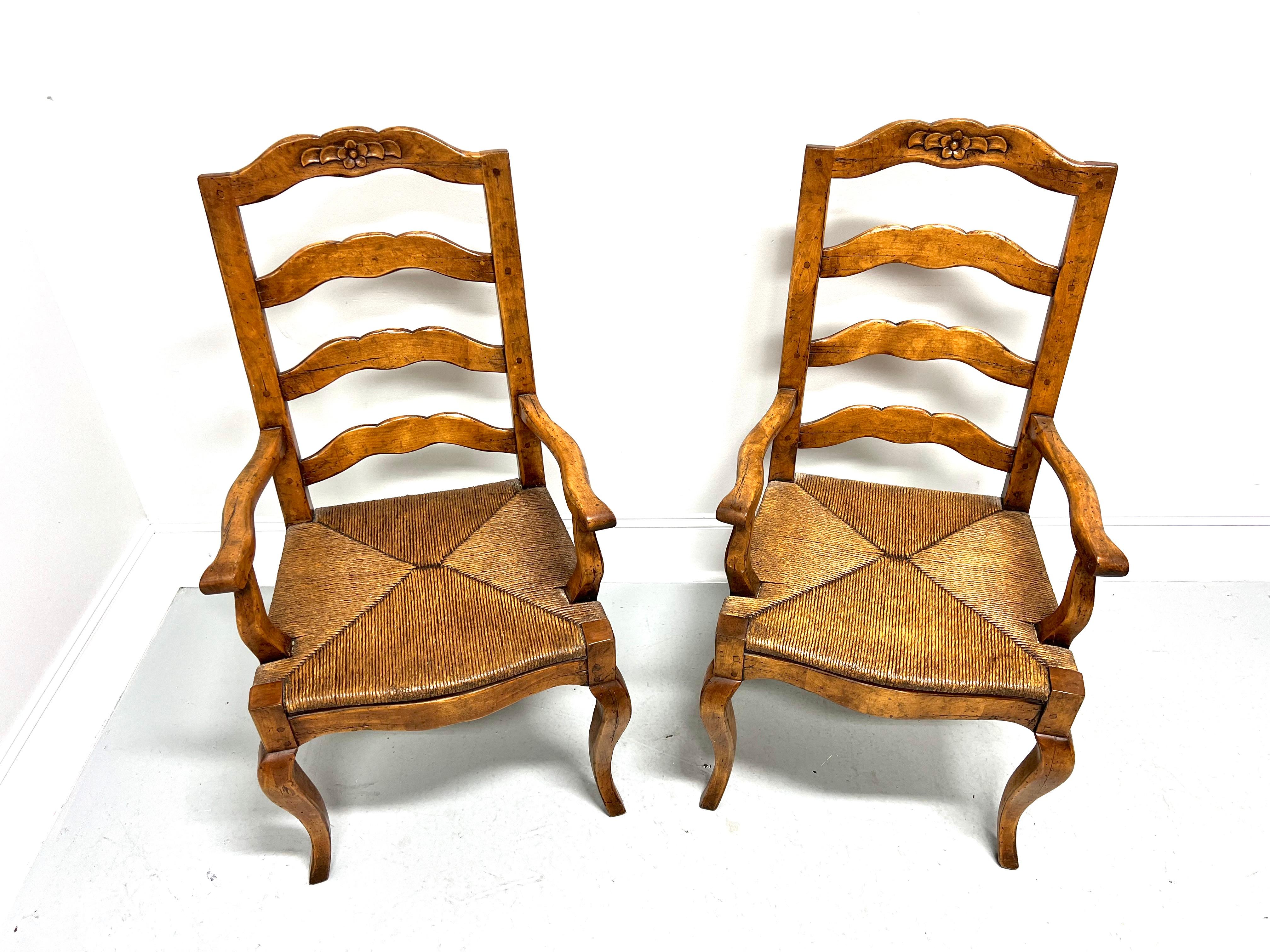 A pair of French Country style dining armchairs, unbranded. Solid nutwood with a distressed finish, ladder back design, decoratively carved crest rail, slightly curved arms with curved supports, rush seats, carved apron, and curved legs. Made in the