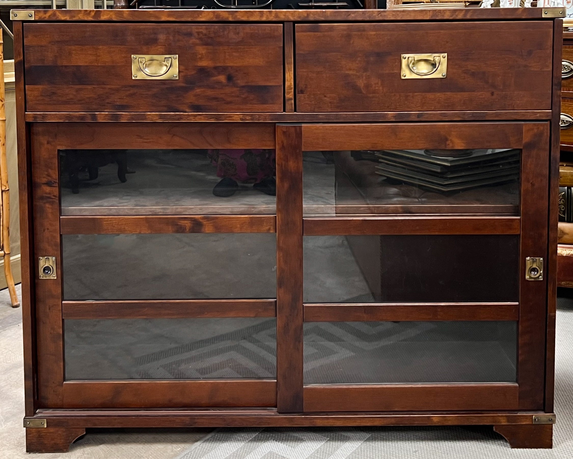 This is an English campaign style mahogany and brass bookcase with sliding doors and two adjustable shelves. It is unmarked and in very good condition.