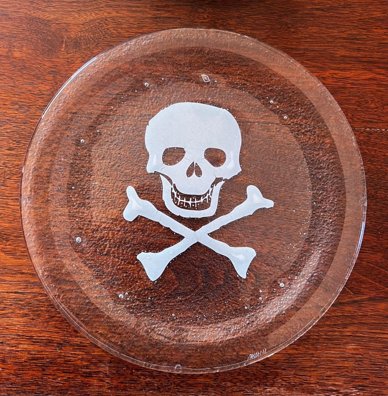 Late 20th C., a set of 8 seeded glass dinner plates with a white skull and crossbones design. These plates are substantial. The skull and crossbone design is incorporated into the seeded glass, not printed on.

Dimensions:
11