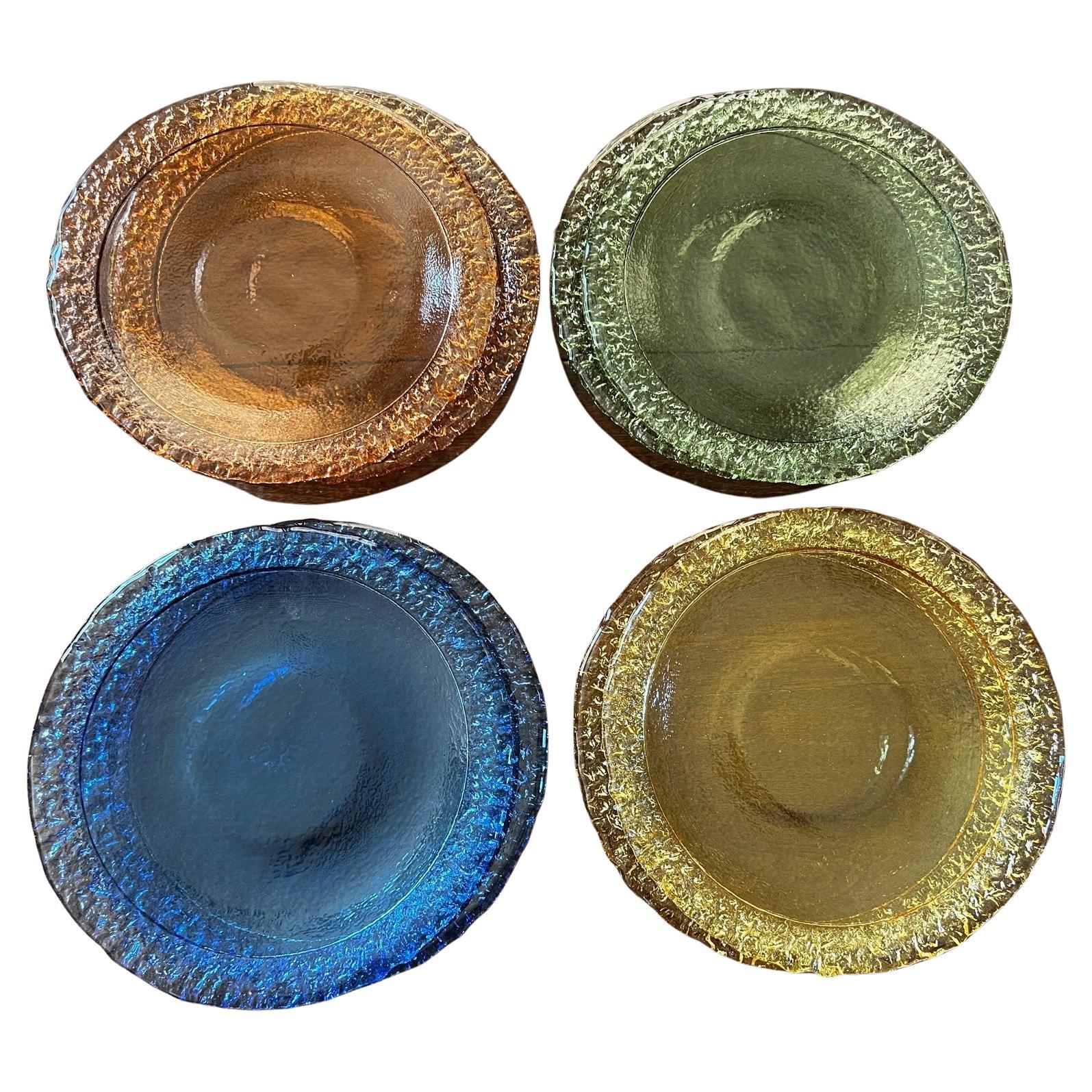 A set of 8 large pressed glass chargers. Two each in yellow, blue, orange and green. The facing side is smooth while the underside is textured. There is a 1.5