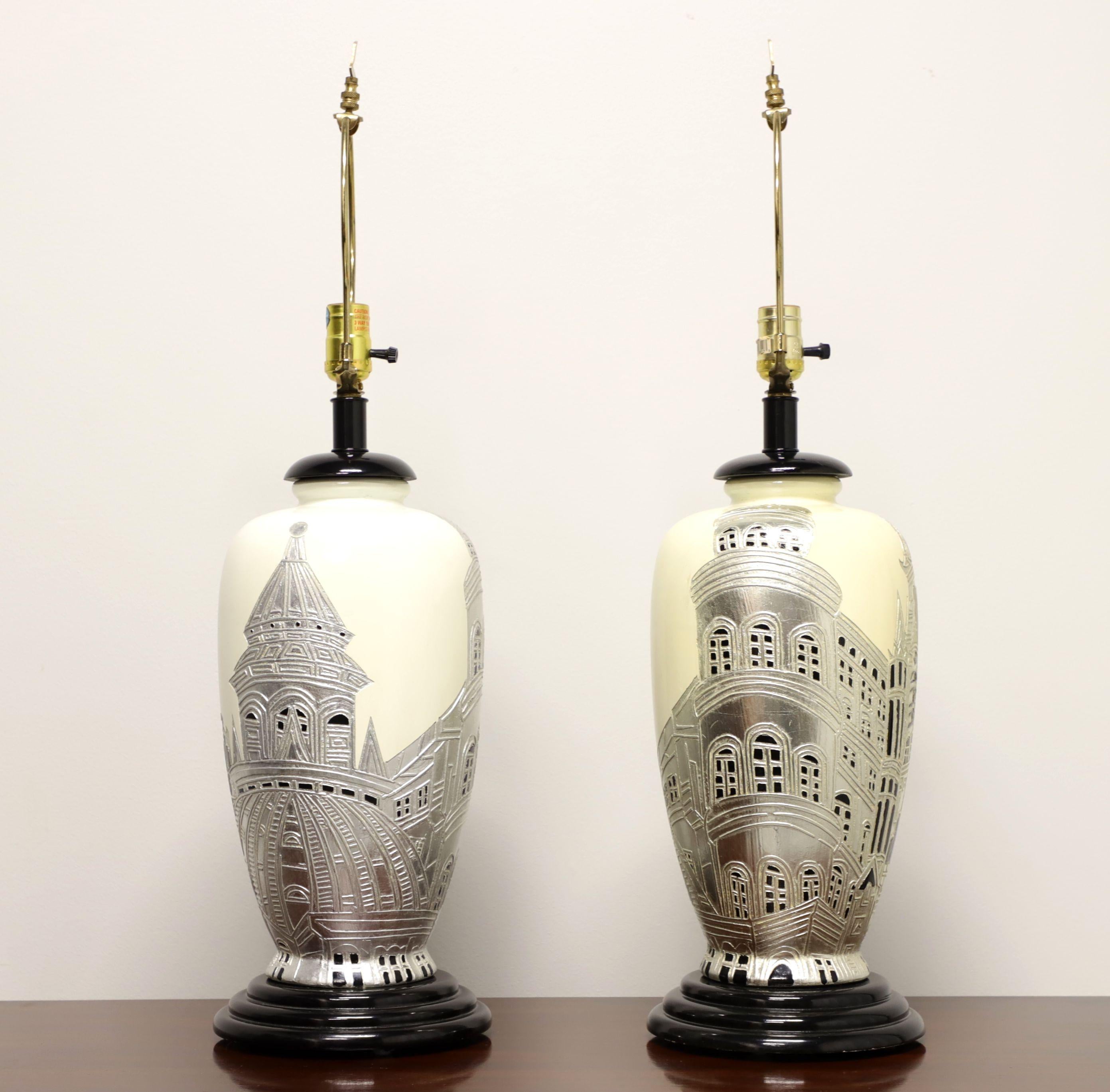 A pair of Asian style table lamps, unbranded. Made of porcelain in an urn style with a creamy white background, silver and black Chinoiserie painted scene, on a black painted wood base. Has metal harps and finials. Single standard bulb socket and
