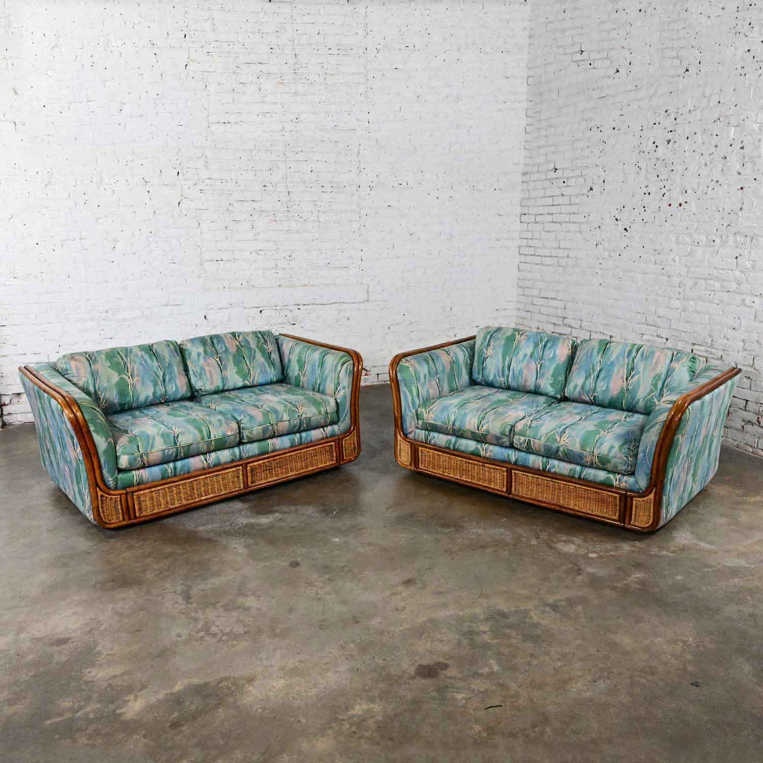 Splendid vintage Boho Chic rattan and wicker tuxedo style upholstered loveseat sofas, a pair. Comprised of rattan & wicker frames and both loveseats wear a beautiful contemporary fabric with colors of blue, green, pink, & white. Beautiful condition,