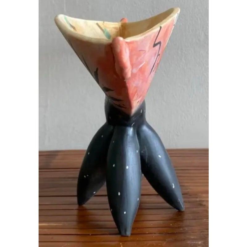 Questa surreale ciotola in ceramica è un'opera d'arte travestita da recipiente. Appollaiato su tre gambe nere a bulbo punteggiate di puntini bianchi, il bacino dipinto a mano si muove in un mix sognante di tonalità corallo, verde acqua e oro. I