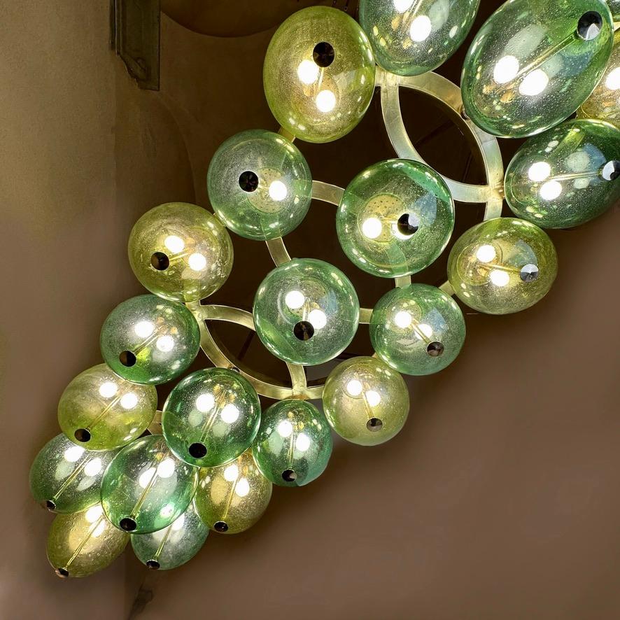 The ringed brass body of the chandelier with two different tones of green Pulegoso Murano art glass boules (held in place with brass large screws) to be put as a center piece in a room or over a long rectangular Pool or a Dining table for a stunning