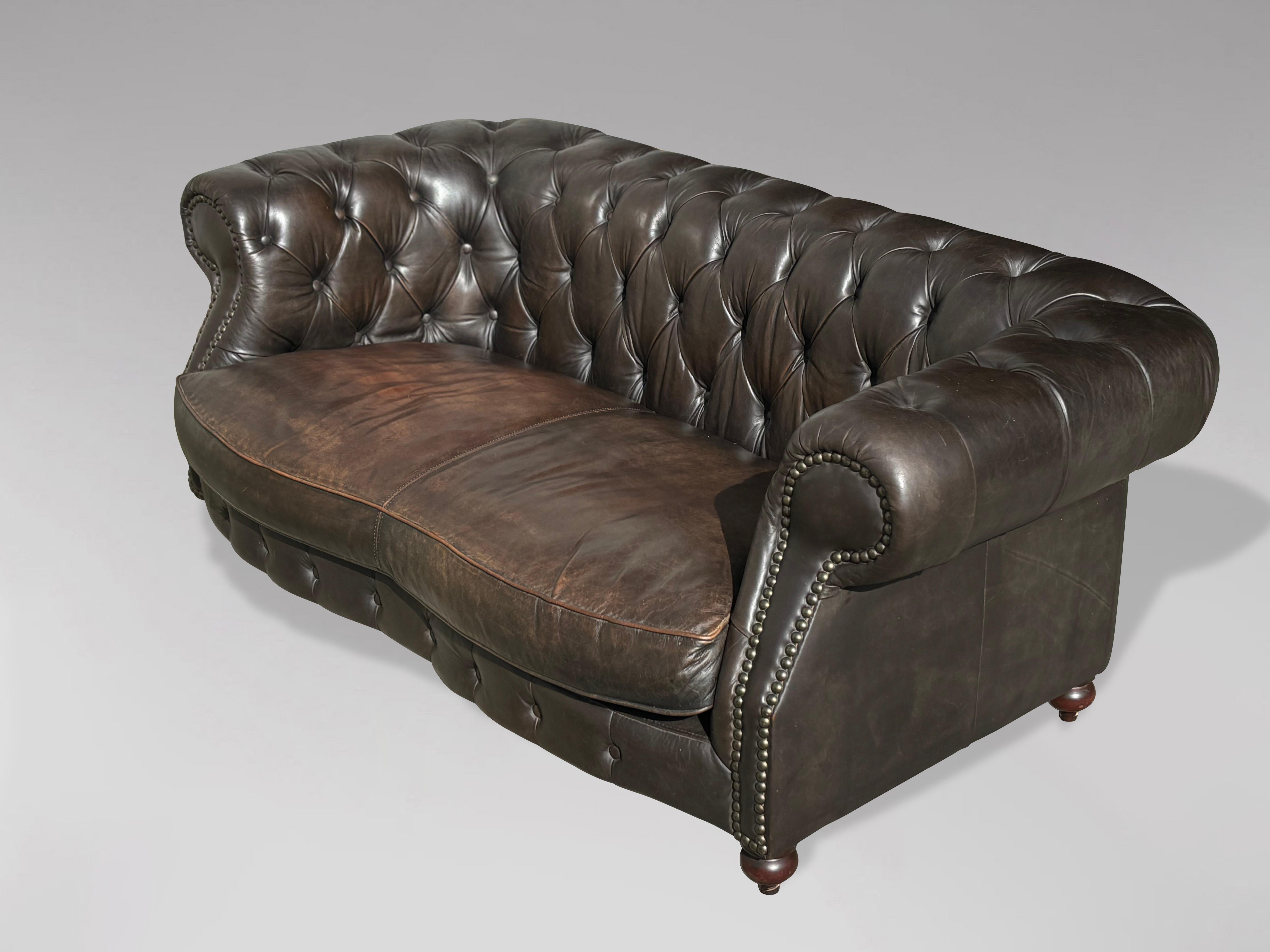 A late 20th-century, two-seater, brown leather, serpentine-shaped Chesterfield sofa with one large, shaped, loose feather cushion. It features a fully buttoned scroll back and armrests, raised on bun feet. The original brown leather hide has been