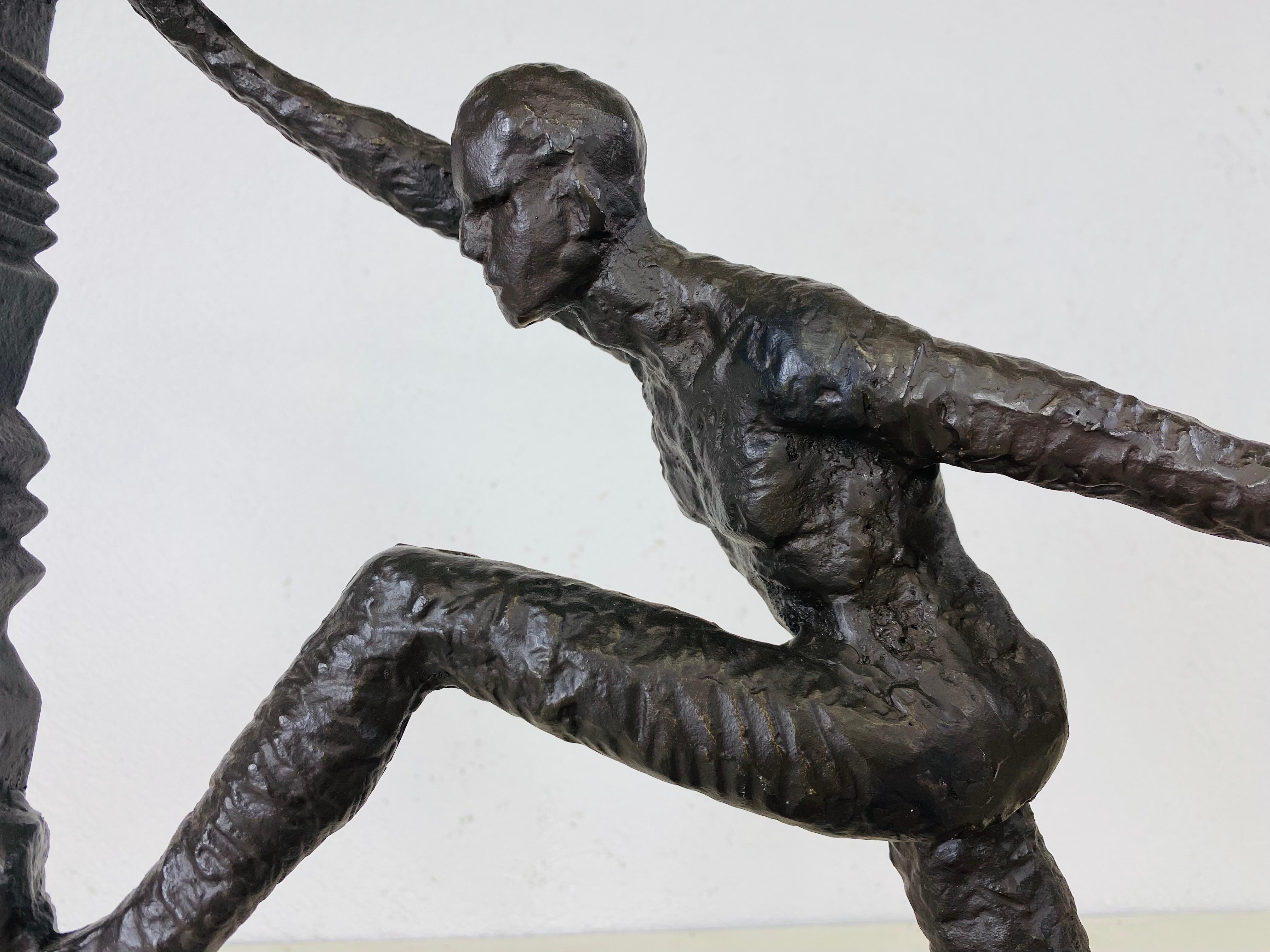 This is a vintage late 20th century cast iron figurative sculpture. The sculpture is in black cast iron and has an abstract quality. This dynamic impressionist male form is encased in a ribbed square box. This sculpture is resting on a black granite