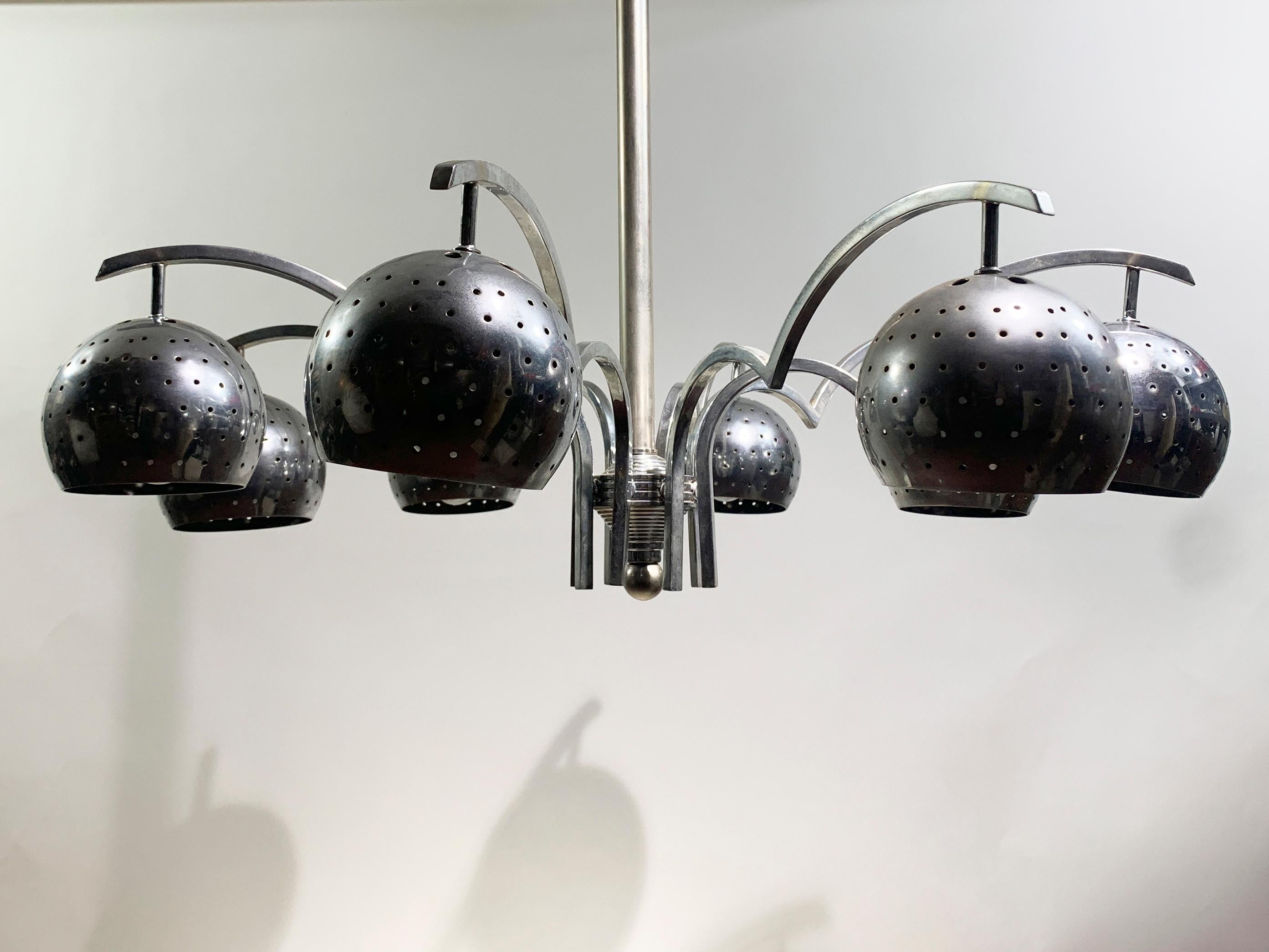 Questo lampadario ha un'estetica audace e moderna con un tocco di design industriale. Presenta un'asta centrale in metallo lucido che si estende dal soffitto e sostiene 8 bracci curvi che si diramano verso l'esterno. Ogni braccio termina con un