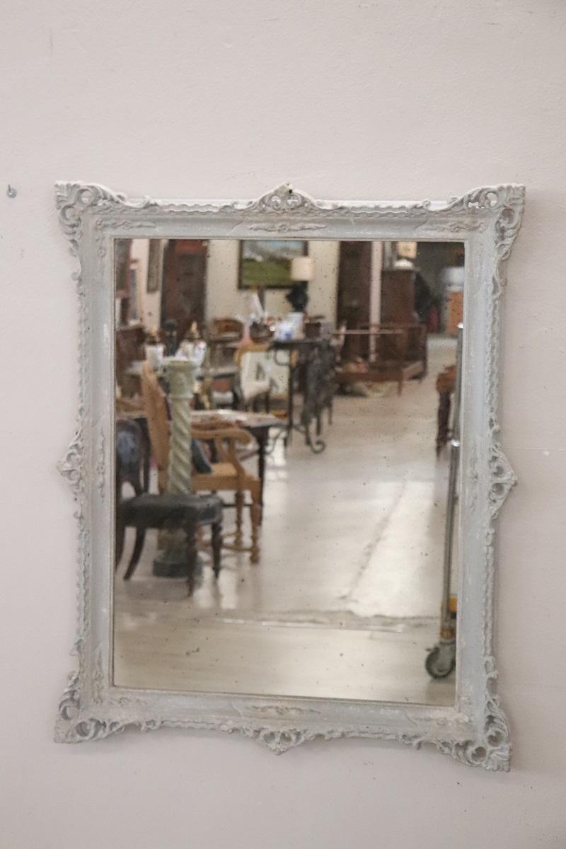 Elegant late 20th century Italian carved poplar wood wall mirror. The frame is characterized by an elaborate decoration with classic taste. The wood is lacquered with a particular artistic technique whose result is very material and with an antiqued