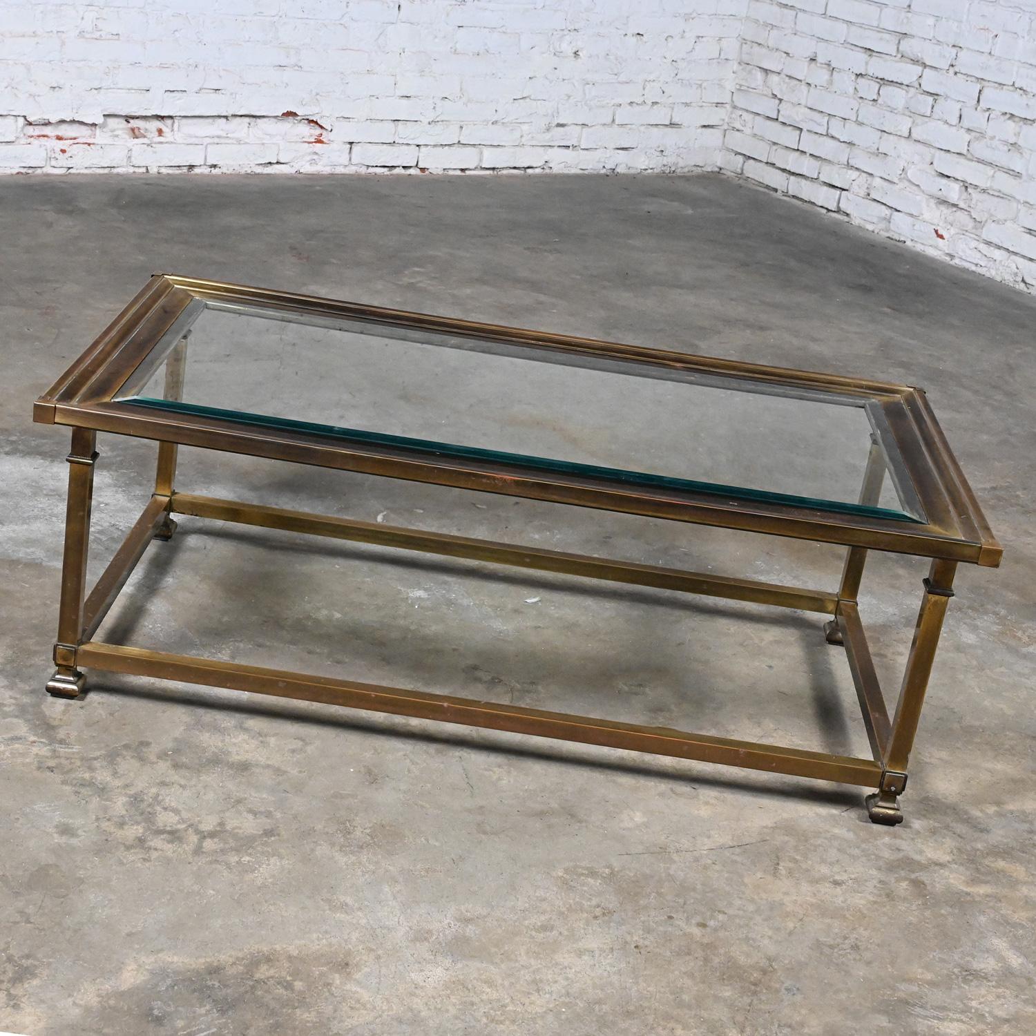 Fabulous vintage coffee table in the style of Mastercraft comprised of a rectangular antiqued brass & purposefully aged patina with steel understructure frame and a ¼ inch thick glass top with 1 inch bevel. Beautiful condition, keeping in mind that
