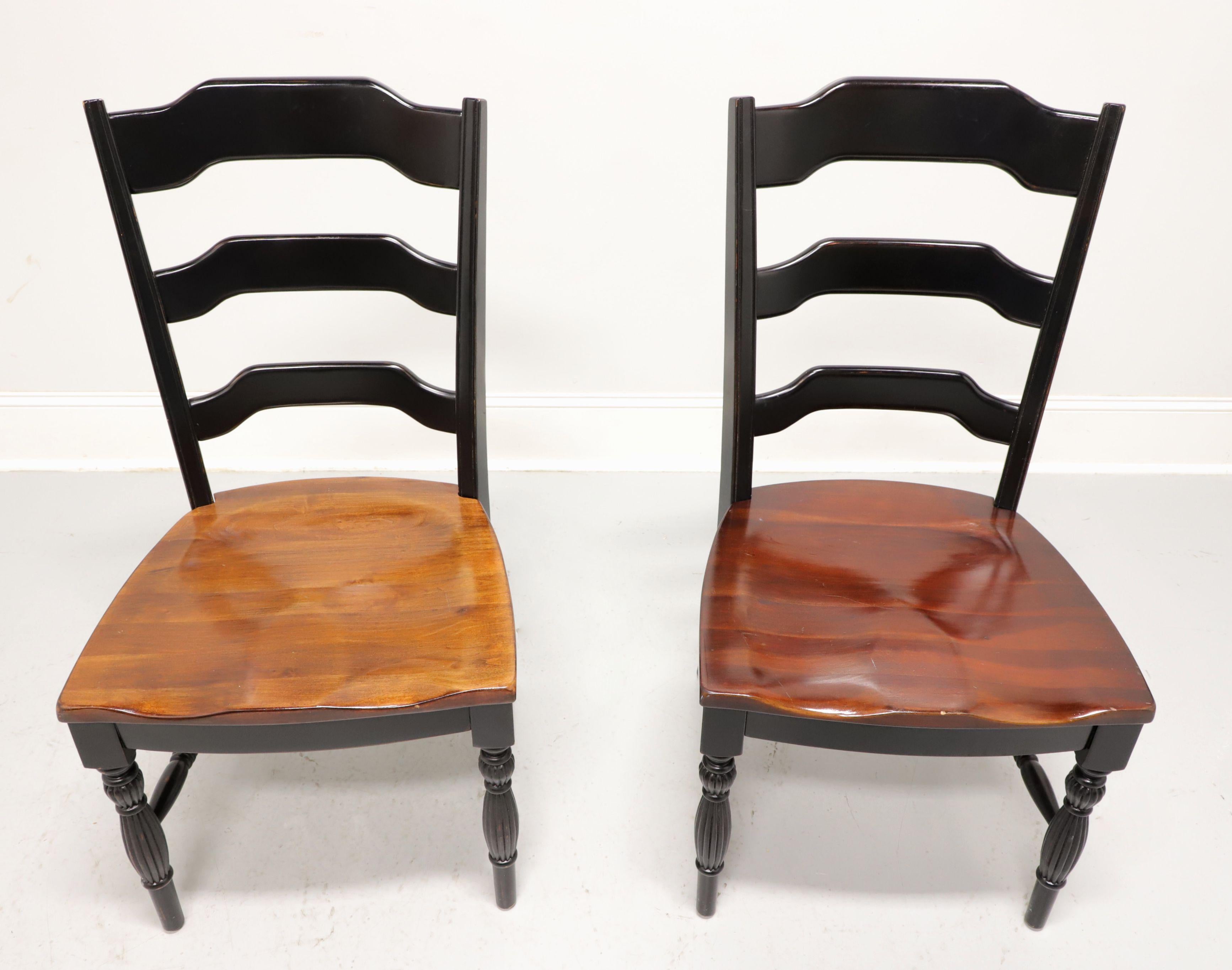 A pair of Cottage / Farmhouse style dining side chairs, unbranded. Hardwood with a distressed black painted finish, carved ladder backs, natural cherry saddle seats, turned & fluted legs and turned stretchers. Made in the Asia, in the late 20th