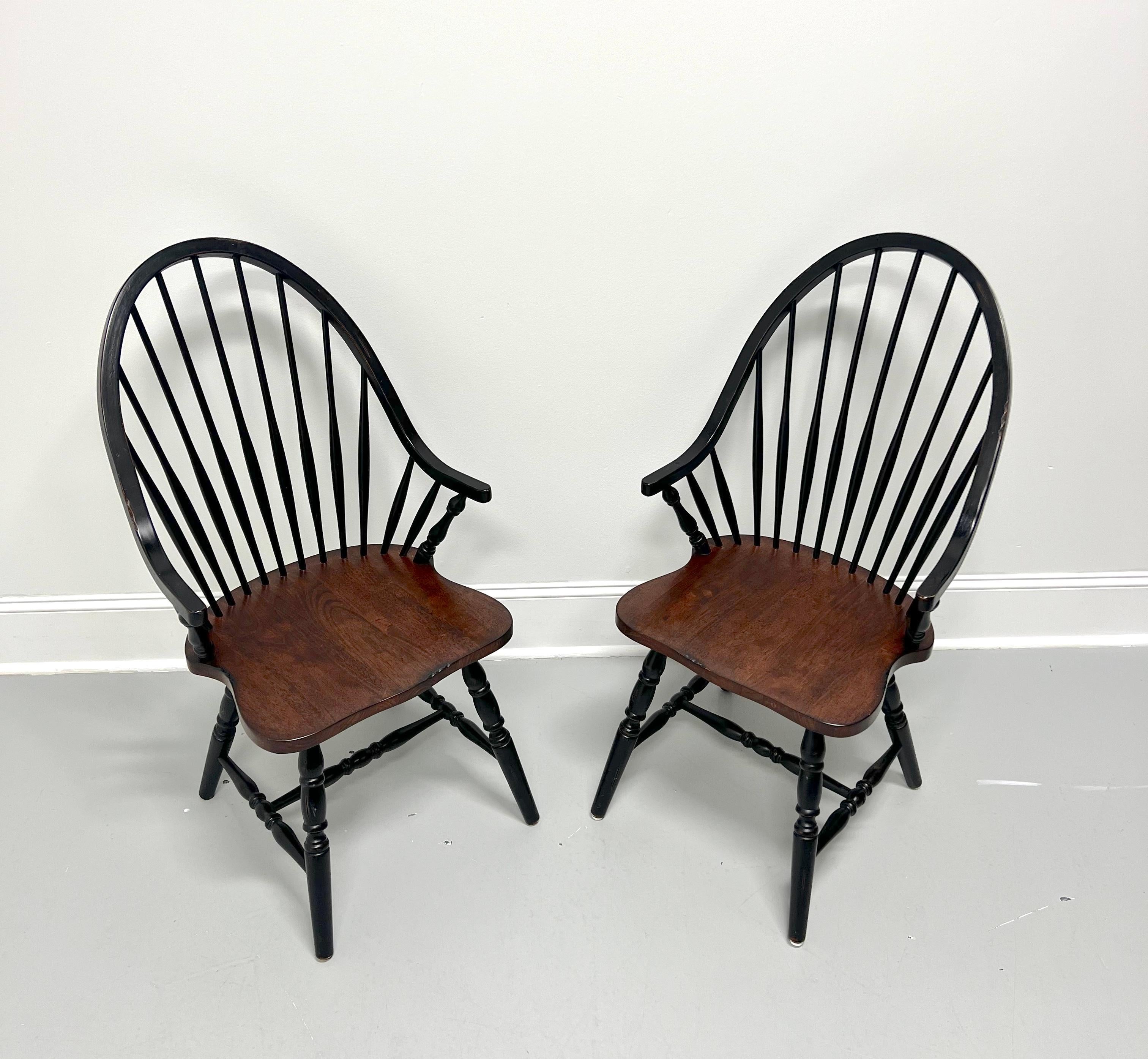 A pair of Windsor dining armchairs, unbranded. Nutwood with back, legs & stretchers painted black, bowback, tapered spindles, short arms with turned supports, solid seat with a distressed stained finish, turned legs, and turned stretchers.  Made in
