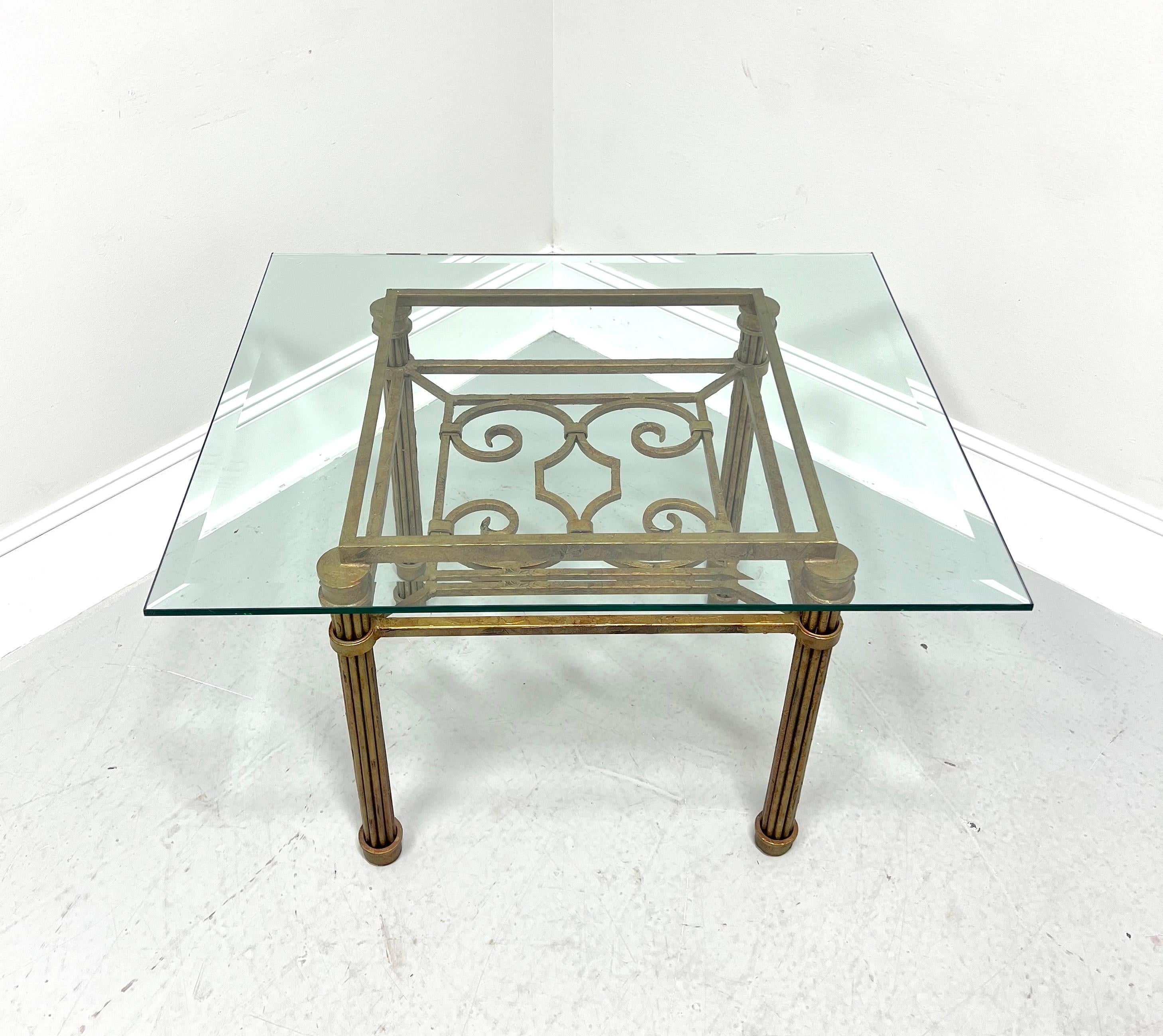 A Contemporary style glass top cocktail table, unbranded. Heavily constructed distressed cast metal base in a square shape, an open decoratively designed undertier, fluted column-like legs, round cap feet, and a rectangular beveled edge glass top.