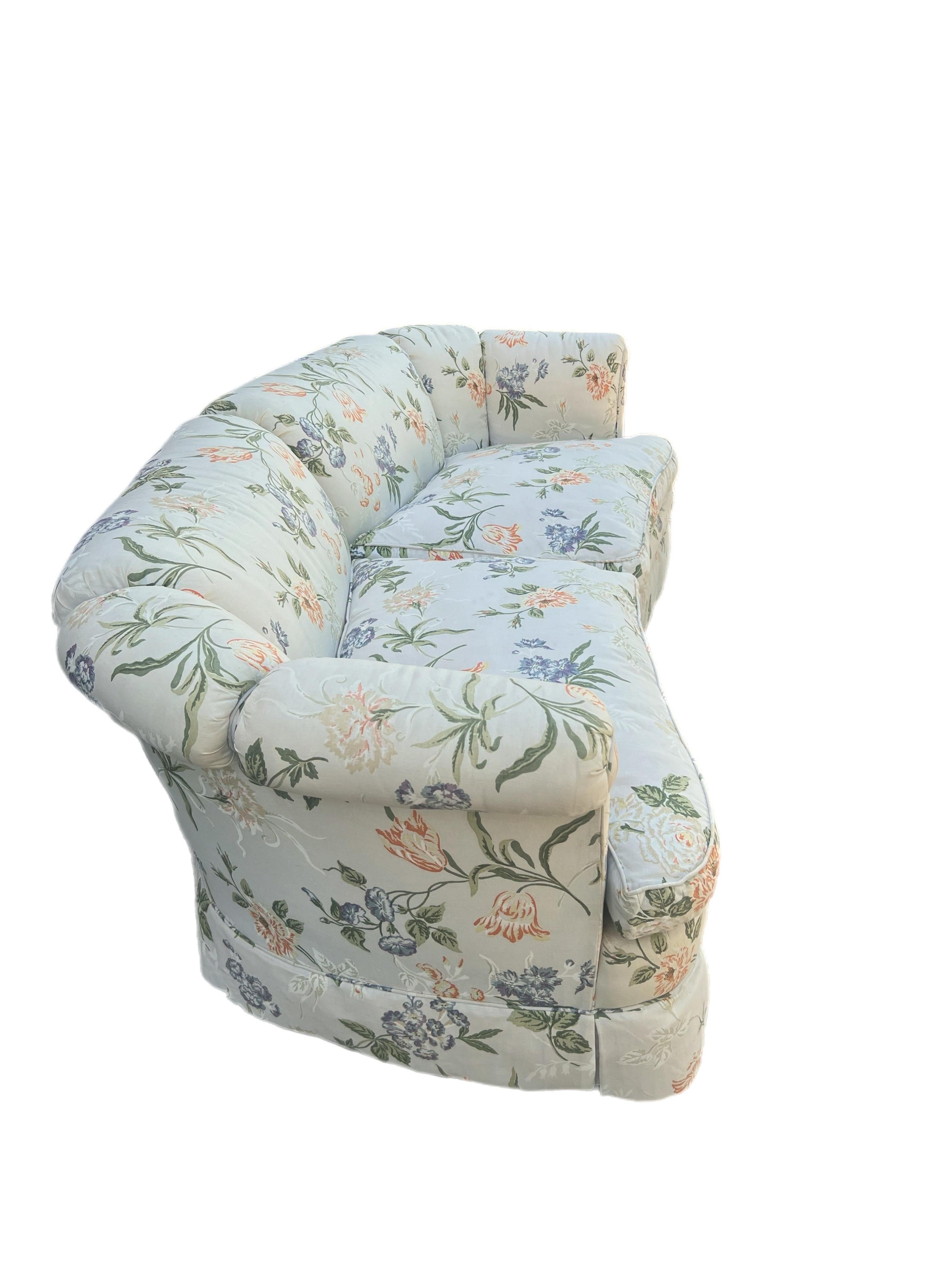 This charming floral sofa exudes a classic elegance, featuring a rounded, low-profile back and plush, well-padded cushions. The upholstery is adorned with a delicate floral pattern in pastel hues of blue, green, peach, and white, creating a serene