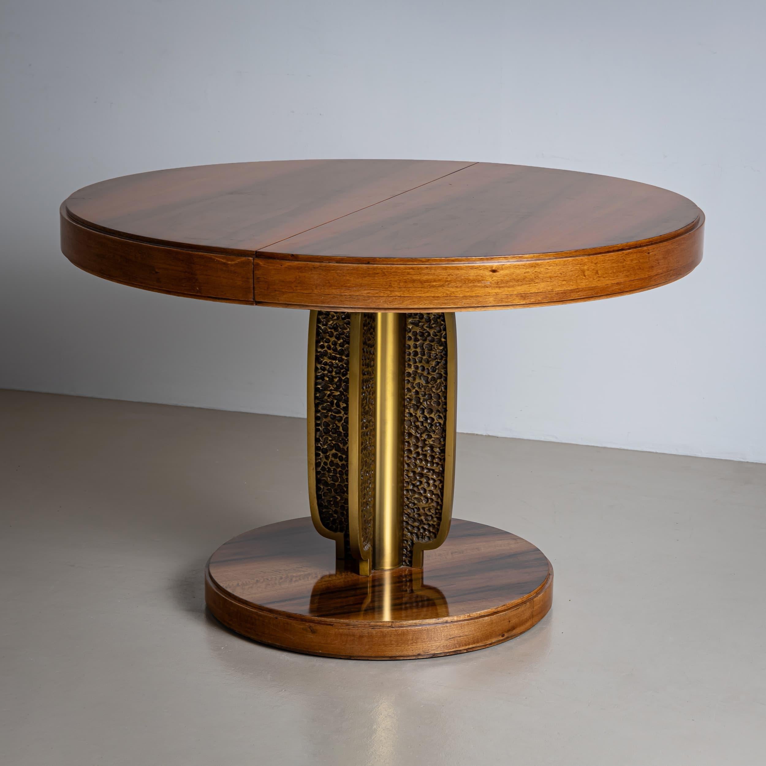 Table à rallonge ronde dotée d'un socle exceptionnel en bronze avec une surface texturée, ajoutant une touche distinctive au design. La table repose sur une plate-forme circulaire et atteint une longueur de 165,5 cm lorsqu'elle est entièrement