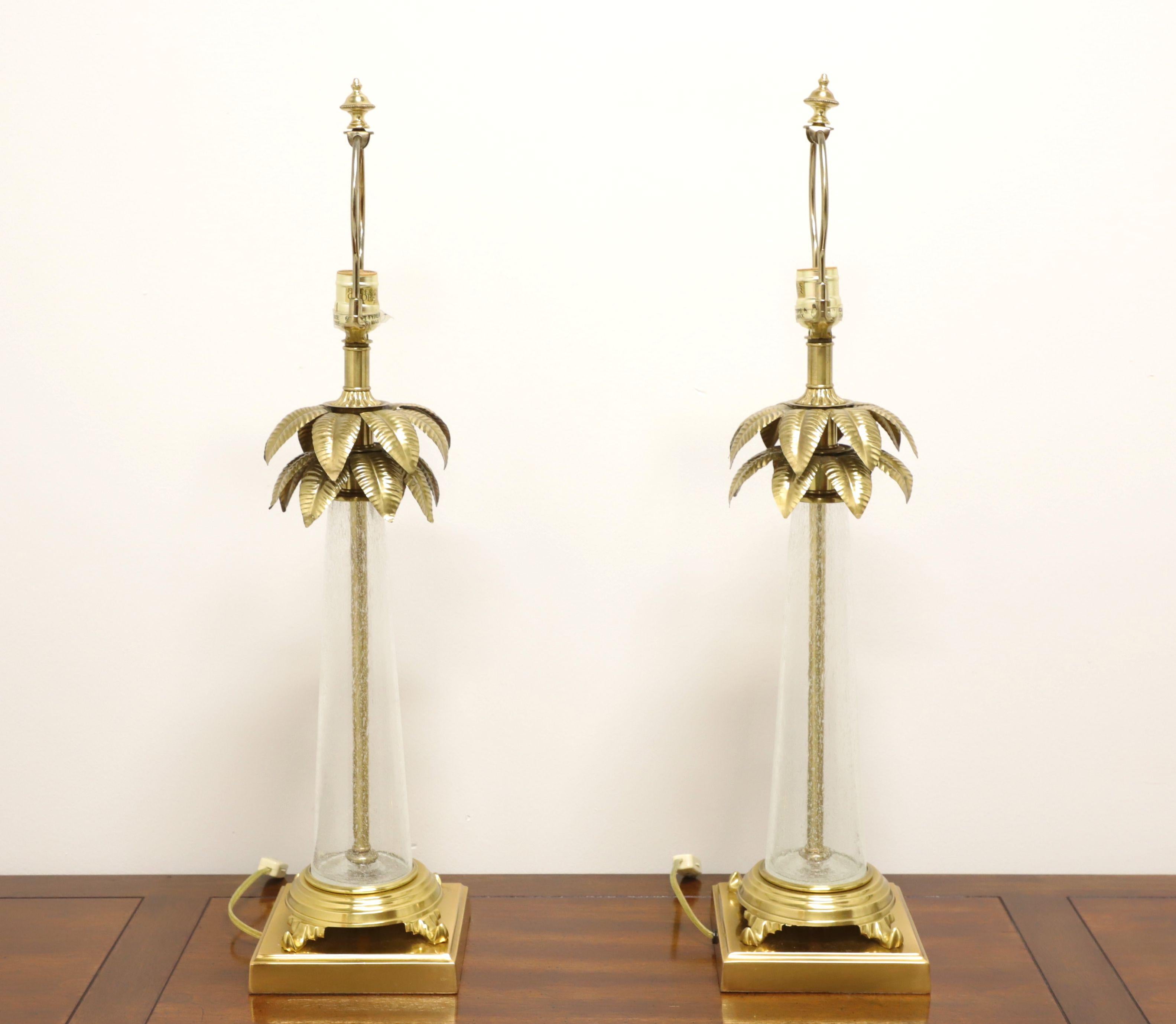A pair of Hollywood Regency style table lamps by Frederick Cooper. Made of solid brass with a bubble glass surround in the shape of a tree trunk with brass palm fronds at lamp neck. Has metal harp and brass finial. Single standard bulb socket and