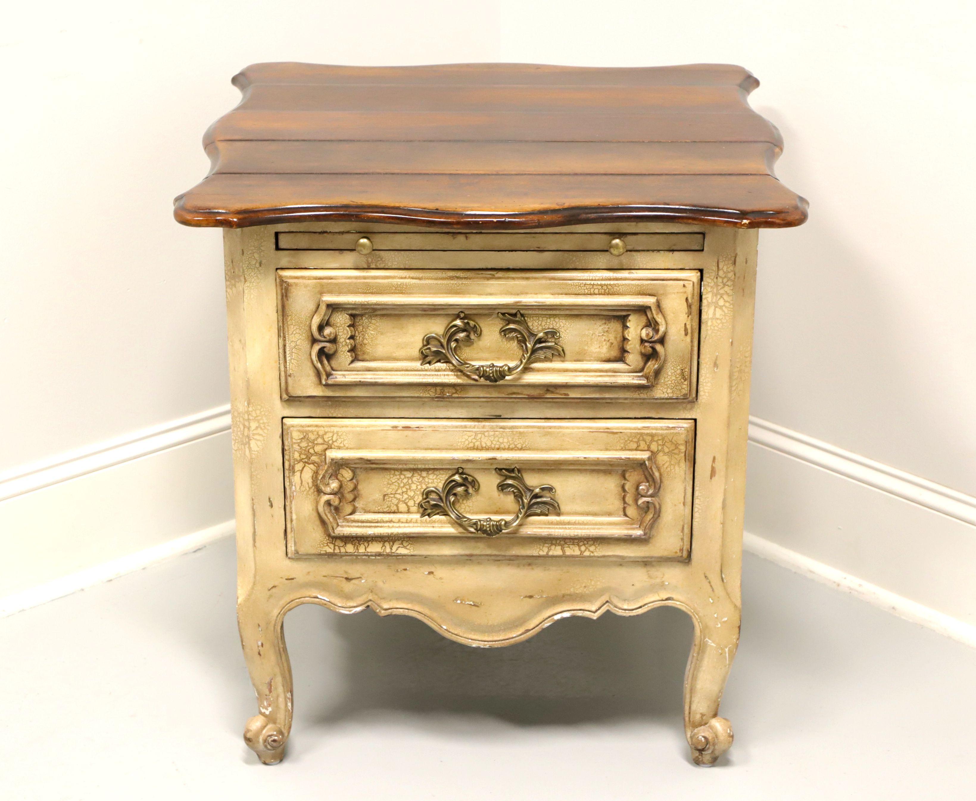 A French Country style nightstand, unbranded. Hardwood painted antique white with a distressed finish to give the appearance of age, dark stained plank style curved top, brass hardware, carved apron & drawer fronts, curved legs and scroll feet.